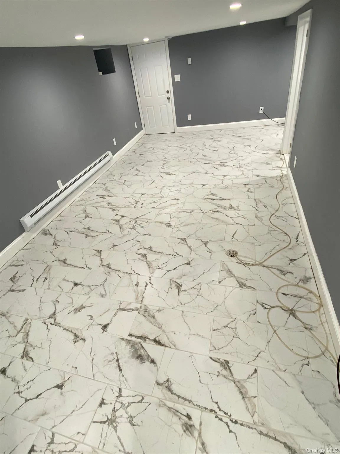 Finished below grade area featuring a baseboard heating unit, light marble finish flooring, and recessed lighting Finished below grade area featuring a baseboard heating unit, light marble finish flooring, and recessed lighting