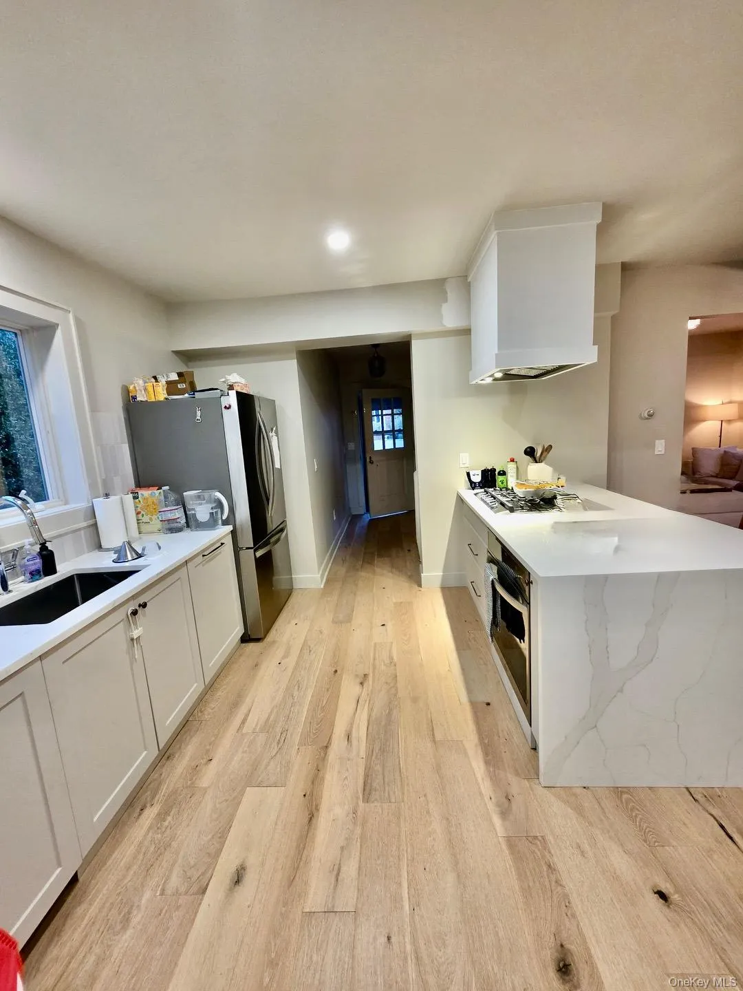Kitchen featuring white cabinets, light stone counters, stainless steel appliances, light wood-style flooring, and a peninsula Kitchen featuring white cabinets, light stone counters, stainless steel appliances, light wood-style flooring, and a peninsula