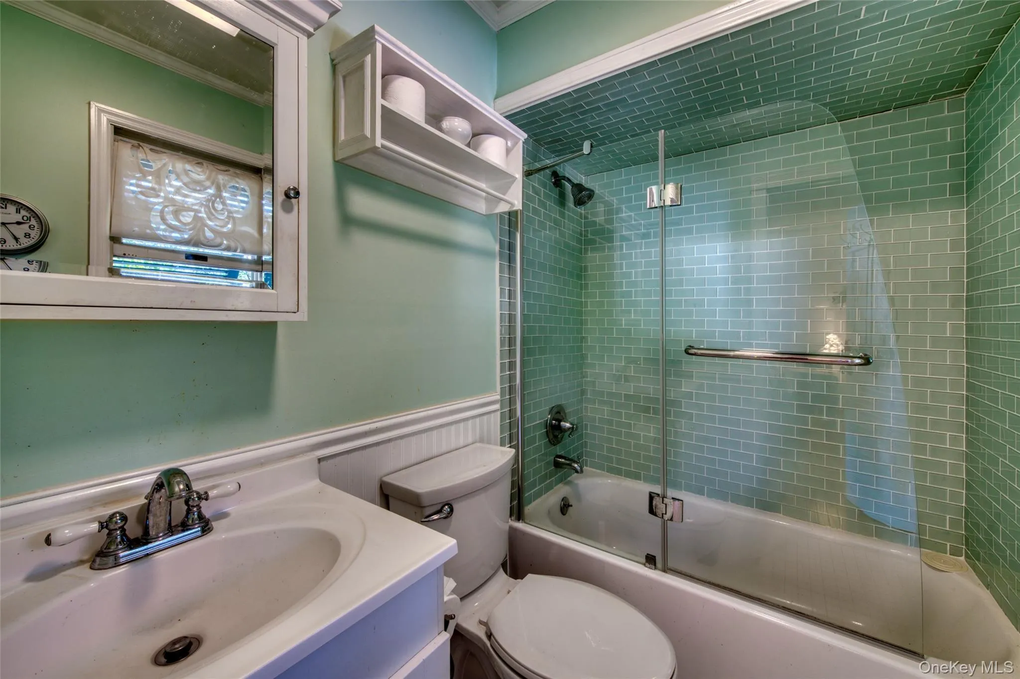 Bathroom with vanity, ornamental molding, a wainscoted wall, and bath / shower combo with glass door Bathroom with vanity, ornamental molding, a wainscoted wall, and bath / shower combo with glass door