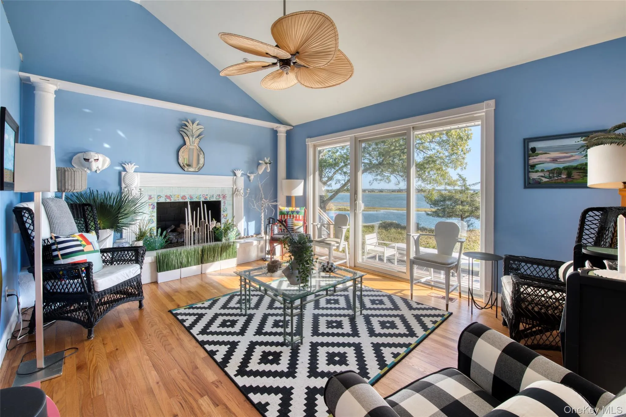 Living area featuring a water view, high vaulted ceiling, light wood-type flooring, a fireplace, and ceiling fan Living area featuring a water view, high vaulted ceiling, light wood-type flooring, a fireplace, and ceiling fan