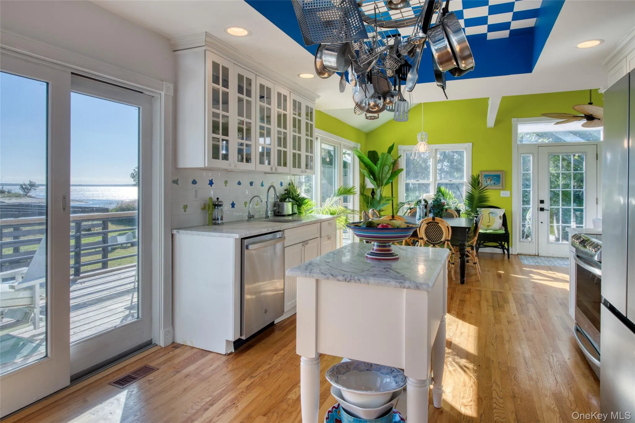 Kitchen with white cabinetry, glass insert cabinets, light wood-style floors, decorative backsplash, and stainless steel appliances Kitchen with white cabinetry, glass insert cabinets, light wood-style floors, decorative backsplash, and stainless steel appliances