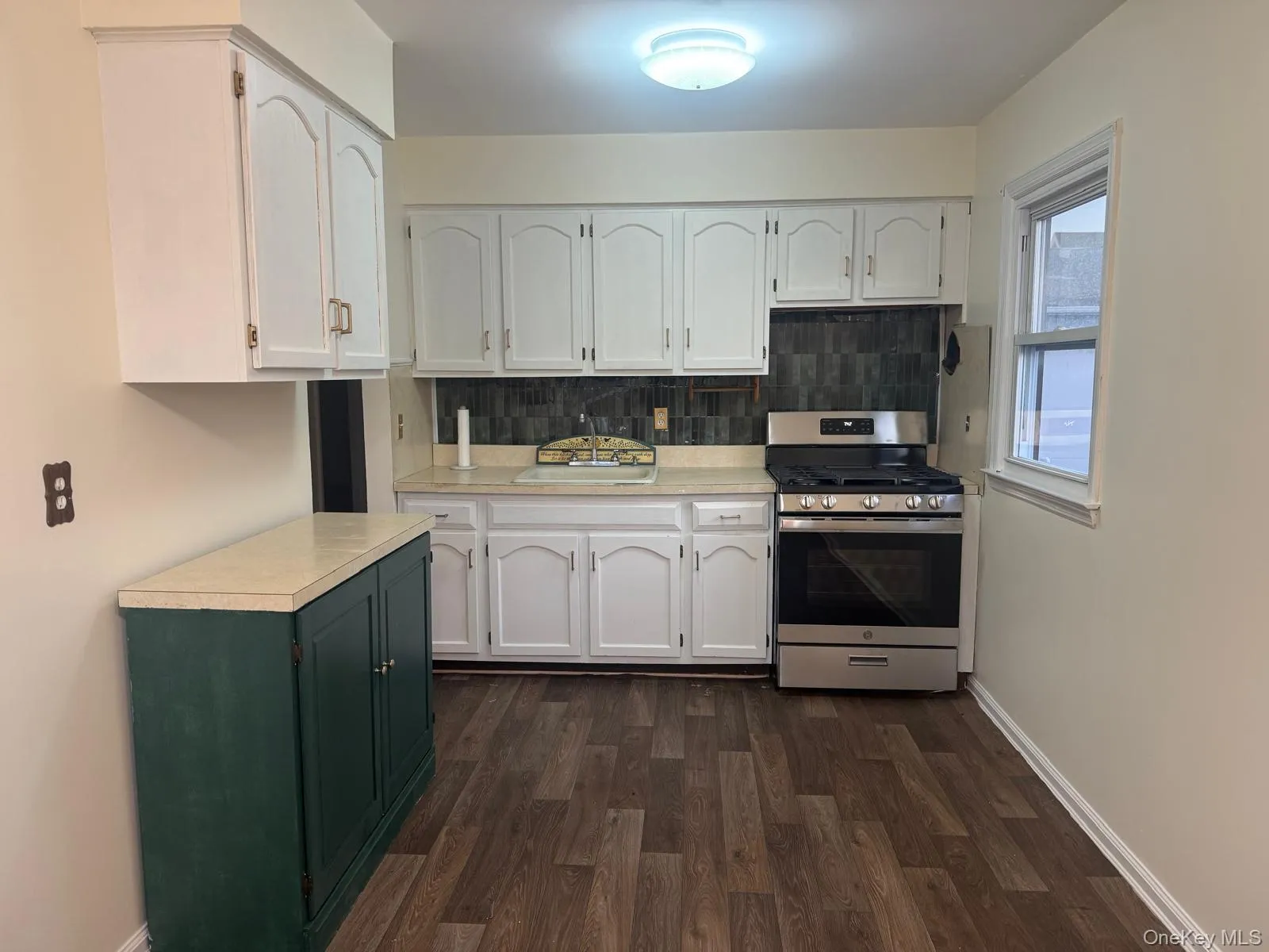 Kitchen featuring gas stove, decorative backsplash, and white cabinets Kitchen featuring gas stove, decorative backsplash, and white cabinets