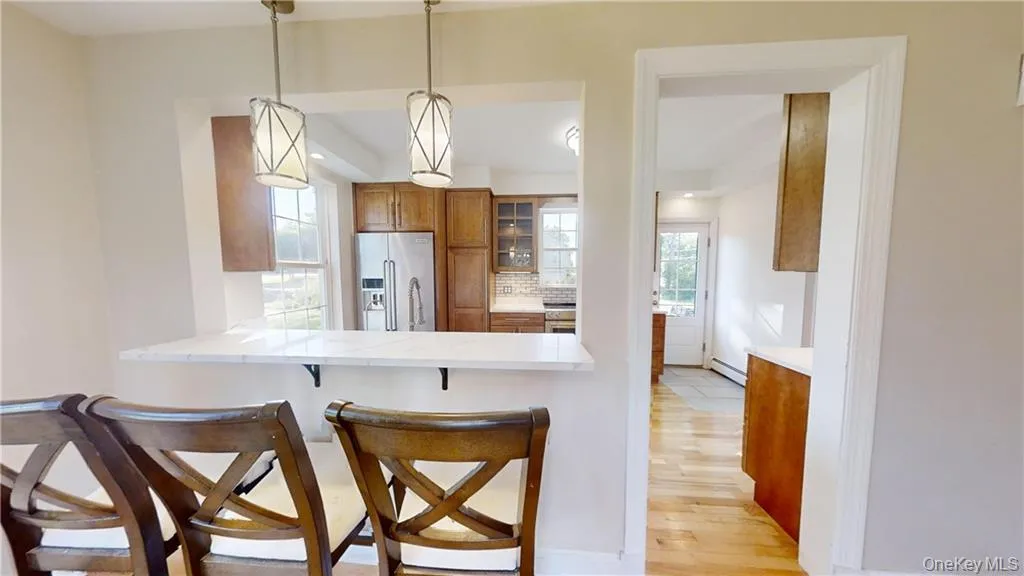 Kitchen featuring hanging light fixtures, brown cabinets, high end fridge, a kitchen breakfast bar, and light wood-style floors Kitchen featuring hanging light fixtures, brown cabinets, high end fridge, a kitchen breakfast bar, and light wood-style floors