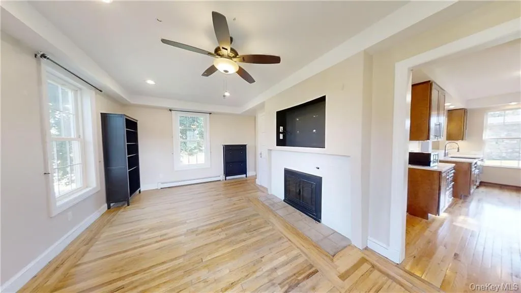 Unfurnished living room featuring ceiling fan, a fireplace, light wood-type flooring, a baseboard heating unit, and recessed lighting Unfurnished living room featuring ceiling fan, a fireplace, light wood-type flooring, a baseboard heating unit, and recessed lighting