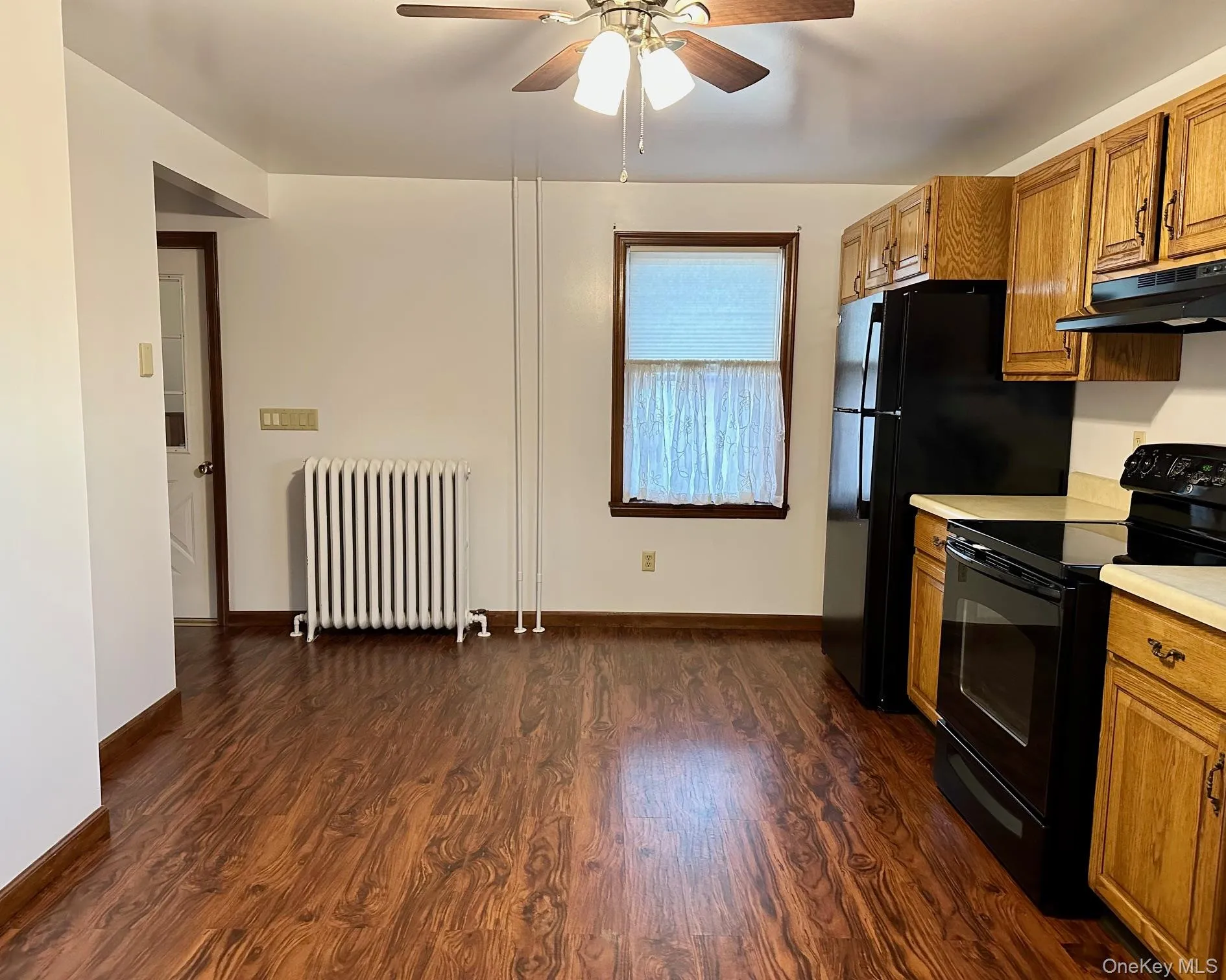 Kitchen featuring black / electric stove, brown cabinetry, light countertops, and radiator Kitchen featuring black / electric stove, brown cabinetry, light countertops, and radiator