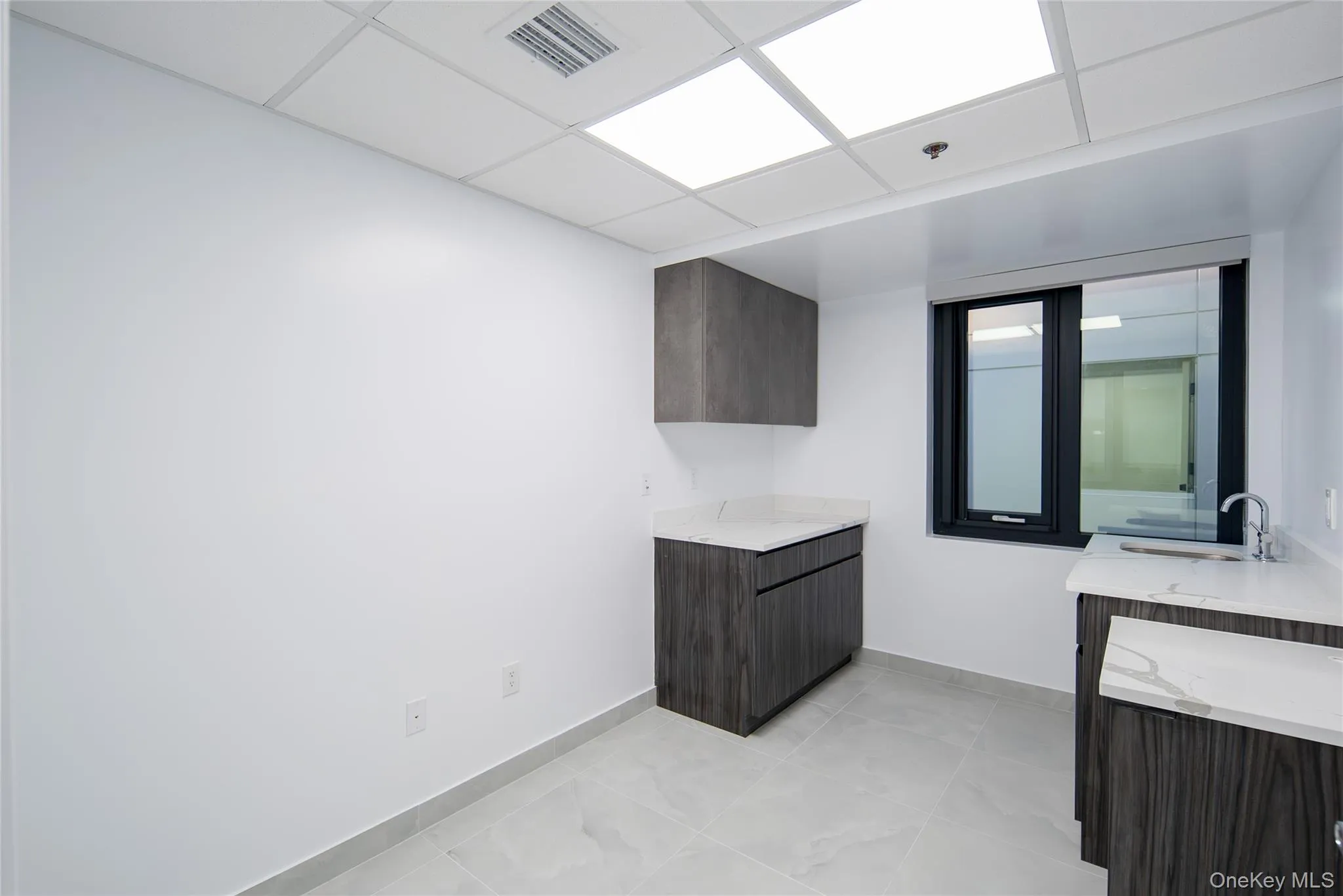 Bar area with dark brown cabinets, a drop ceiling, light stone counters, modern cabinets, and light tile patterned floors Bar area with dark brown cabinets, a drop ceiling, light stone counters, modern cabinets, and light tile patterned floors