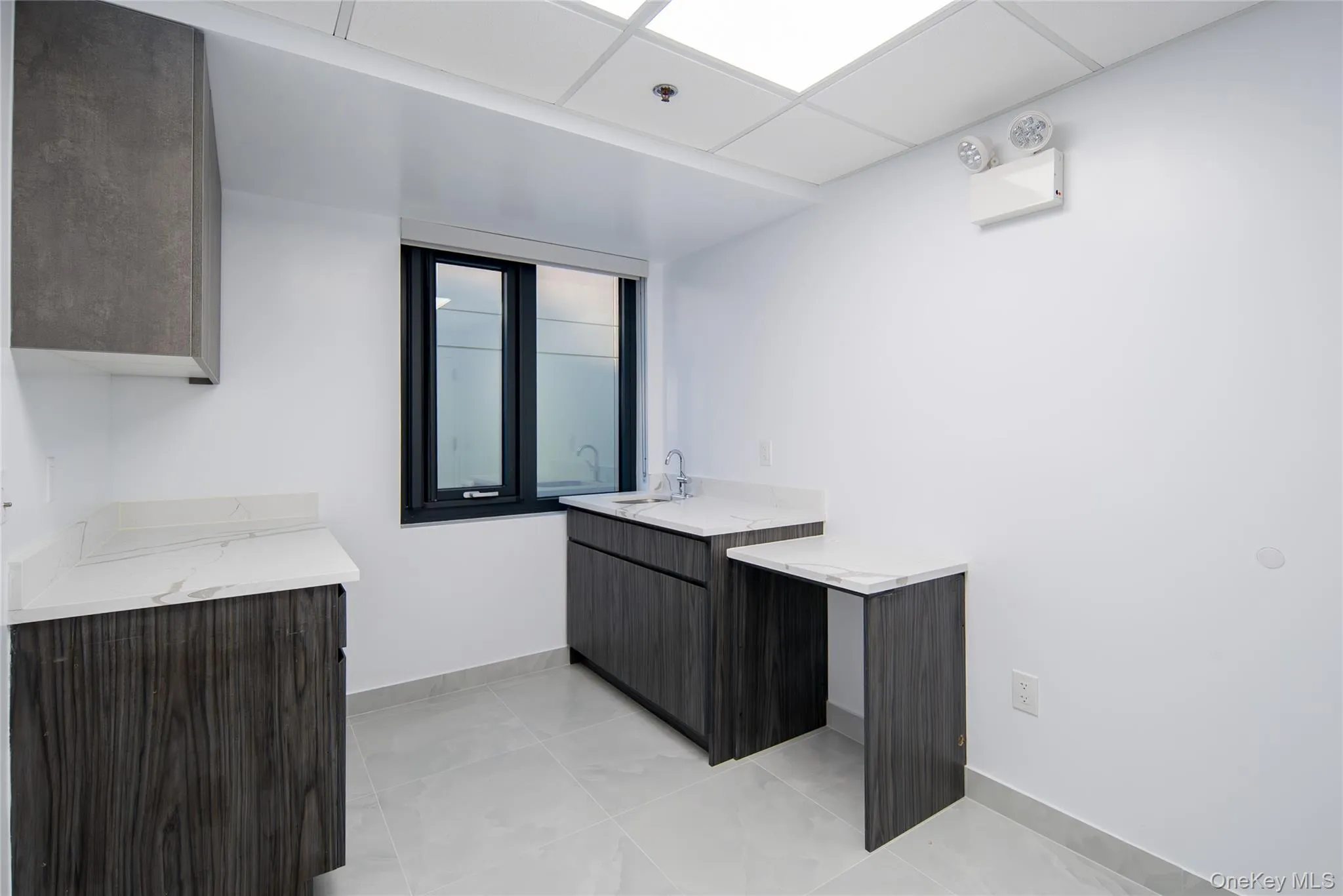 Kitchen featuring a paneled ceiling, light tile patterned floors, modern cabinets, light stone countertops, and dark brown cabinetry Kitchen featuring a paneled ceiling, light tile patterned floors, modern cabinets, light stone countertops, and dark brown cabinetry