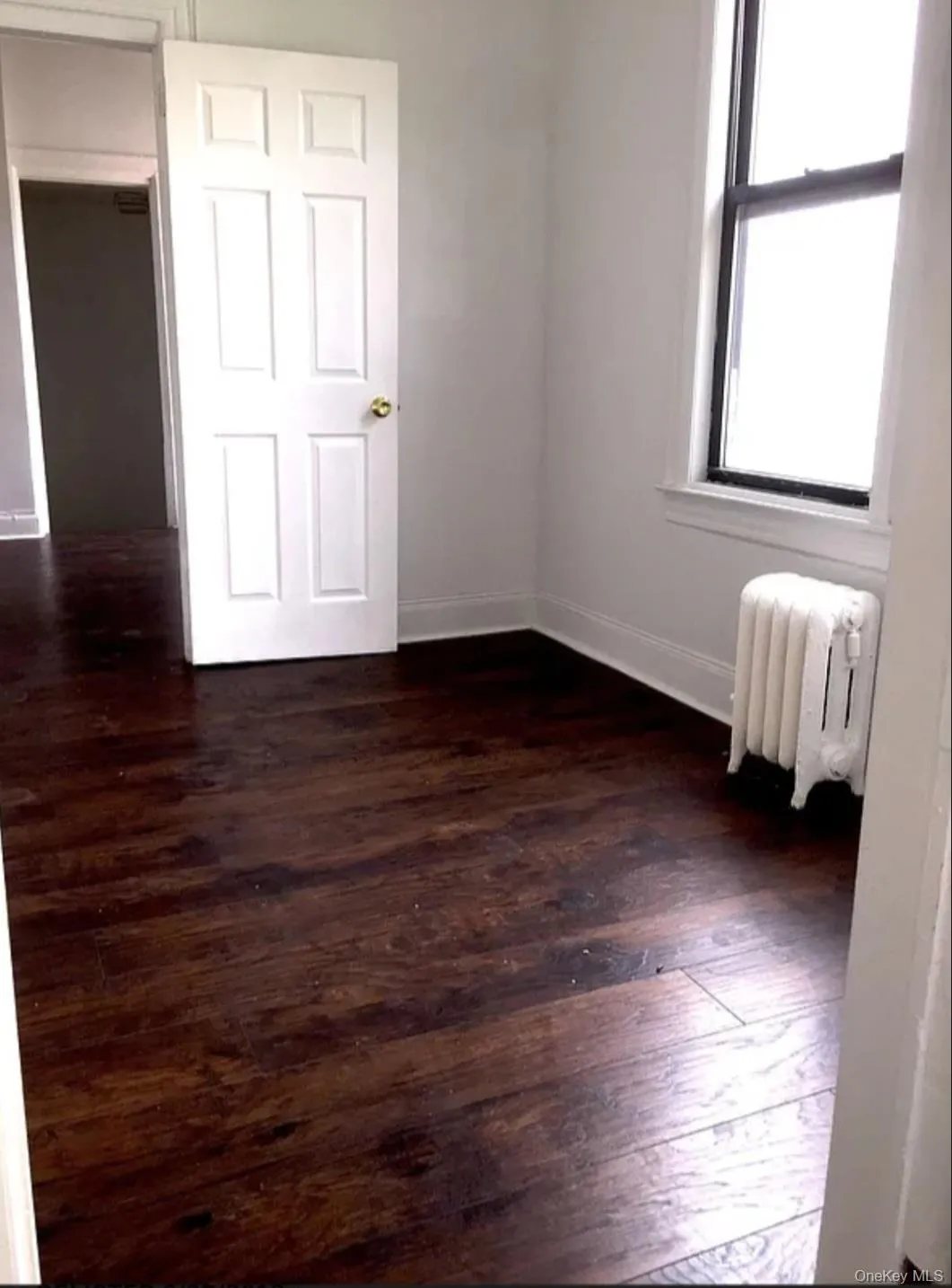 Unfurnished bedroom with dark wood-style flooring and radiator Unfurnished bedroom with dark wood-style flooring and radiator
