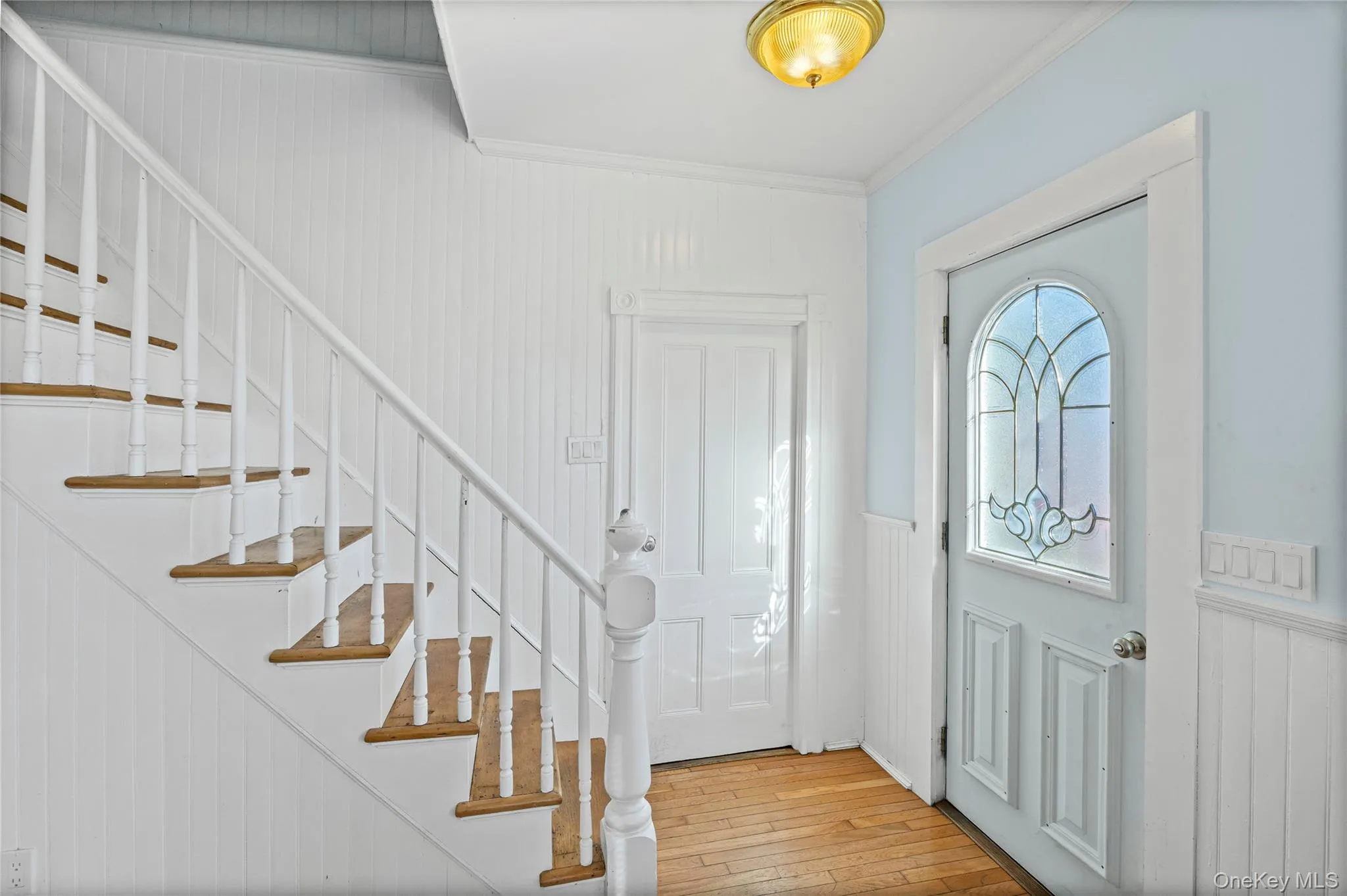 Entryway with a wainscoted wall, ornamental molding, a decorative wall, light wood-style floors, and stairs Entryway with a wainscoted wall, ornamental molding, a decorative wall, light wood-style floors, and stairs