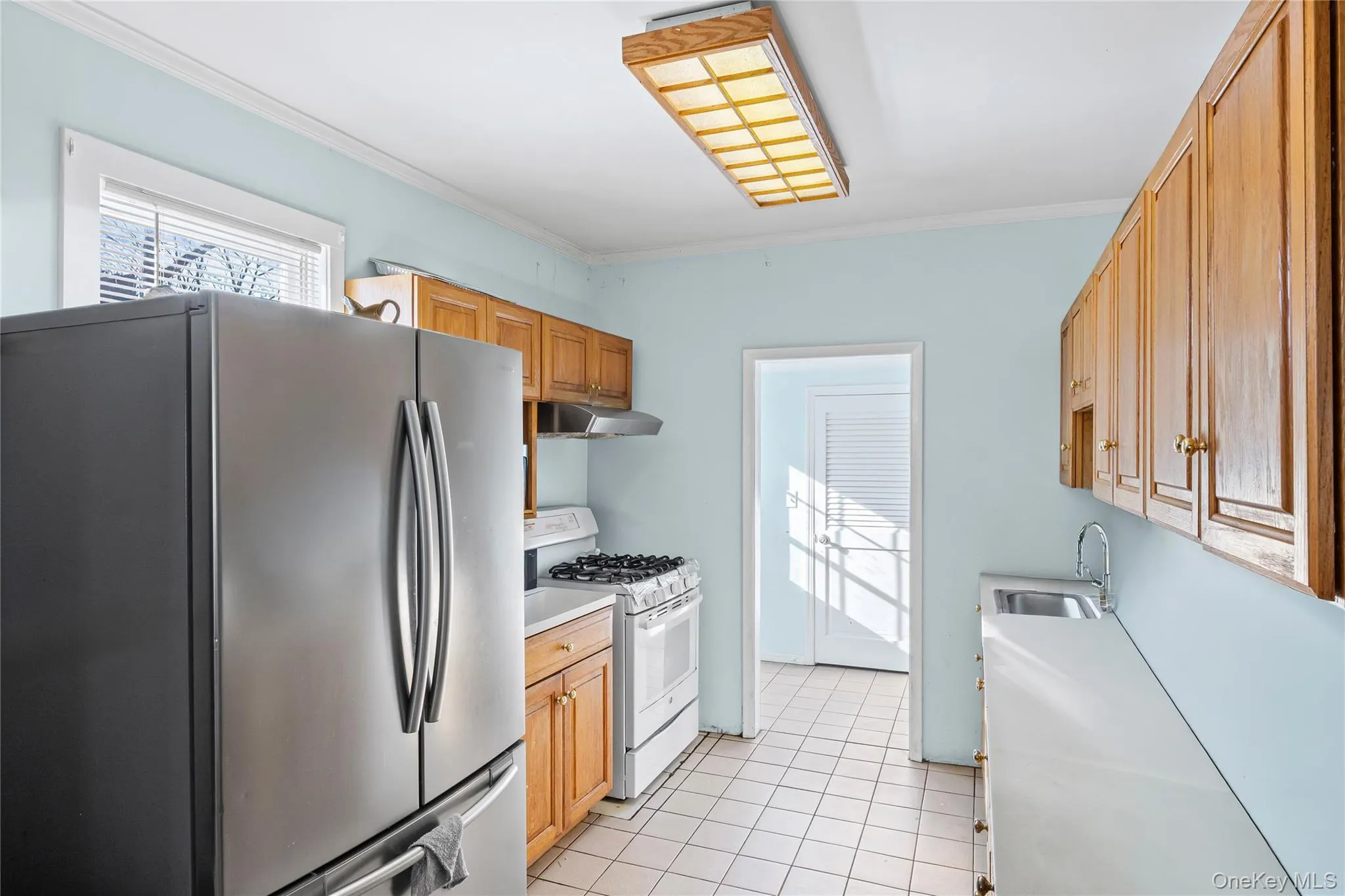 Kitchen featuring freestanding refrigerator, white range with gas stovetop, light countertops, crown molding, and light tile patterned flooring Kitchen featuring freestanding refrigerator, white range with gas stovetop, light countertops, crown molding, and light tile patterned flooring