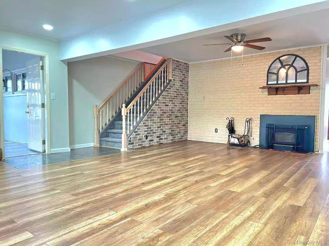 Unfurnished living room with brick wall, wood finished floors, stairs, a fireplace, and a ceiling fan Unfurnished living room with brick wall, wood finished floors, stairs, a fireplace, and a ceiling fan