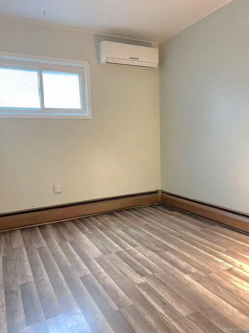Unfurnished room with light wood-type flooring, a baseboard heating unit, and an AC wall unit Unfurnished room with light wood-type flooring, a baseboard heating unit, and an AC wall unit