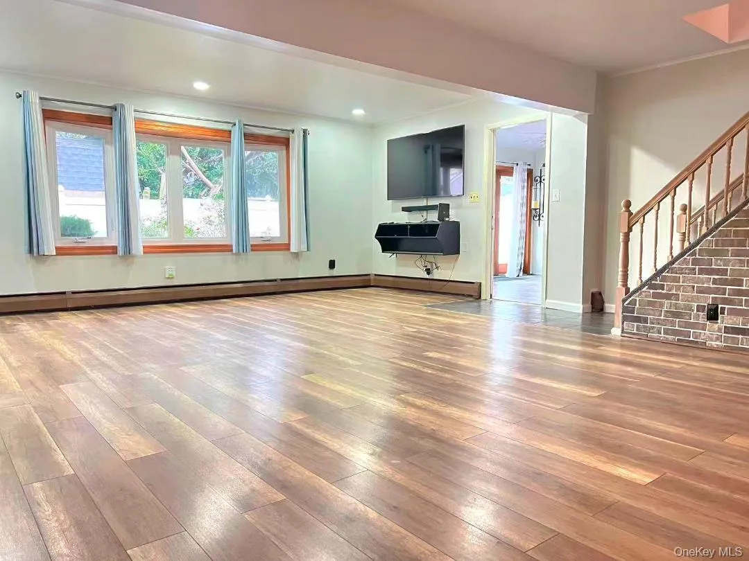 Unfurnished living room with light wood-type flooring, stairway, a baseboard radiator, crown molding, and recessed lighting Unfurnished living room with light wood-type flooring, stairway, a baseboard radiator, crown molding, and recessed lighting