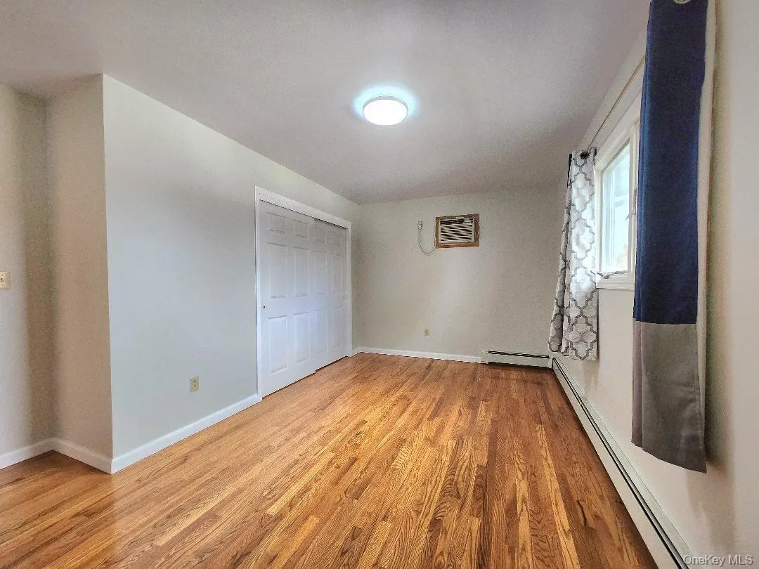 Unfurnished bedroom featuring a baseboard heating unit, light wood-style floors, a closet, and a wall mounted AC Unfurnished bedroom featuring a baseboard heating unit, light wood-style floors, a closet, and a wall mounted AC