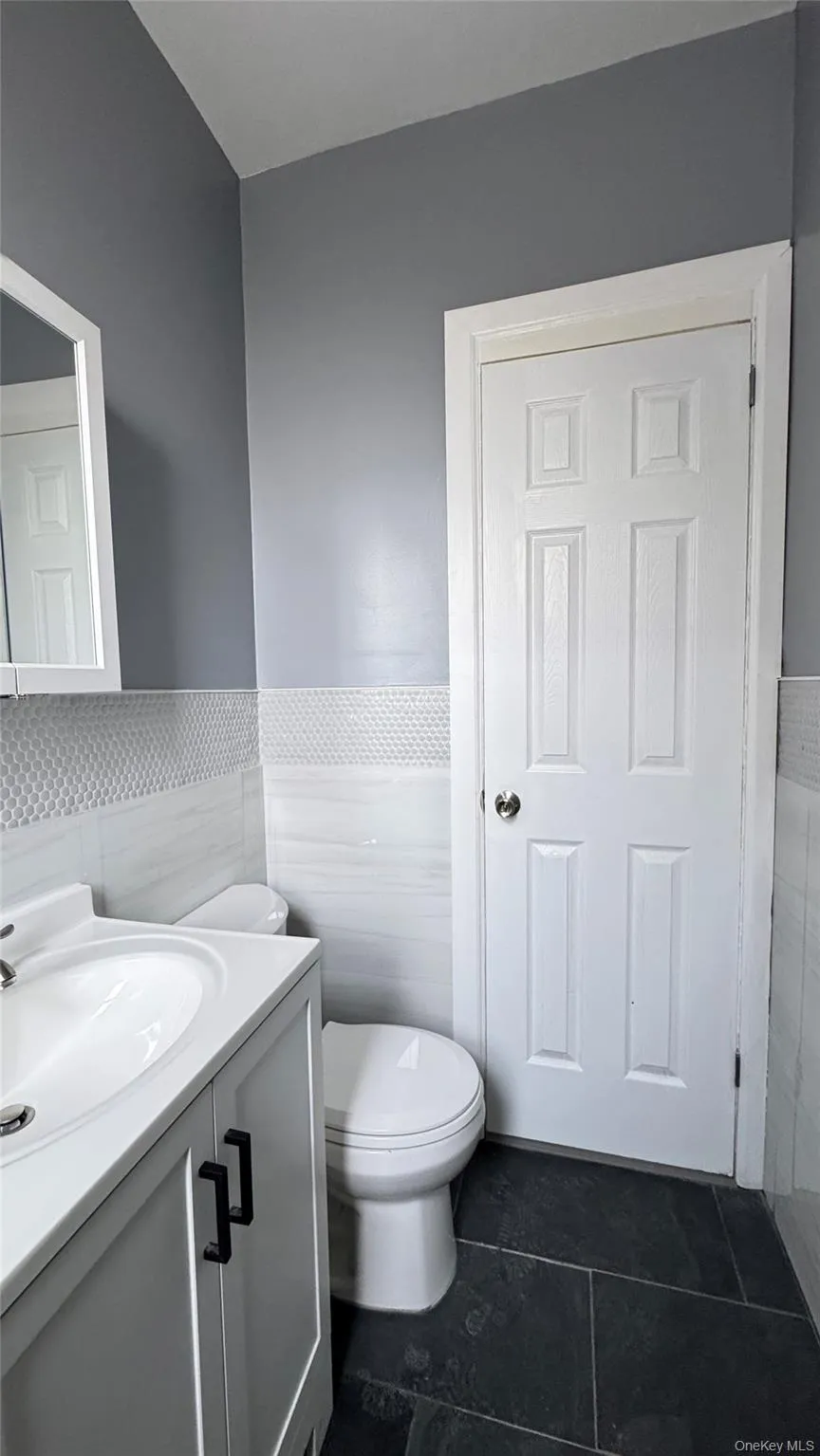 Bathroom featuring a wainscoted wall, vanity, tile walls, and dark tile patterned floors Bathroom featuring a wainscoted wall, vanity, tile walls, and dark tile patterned floors