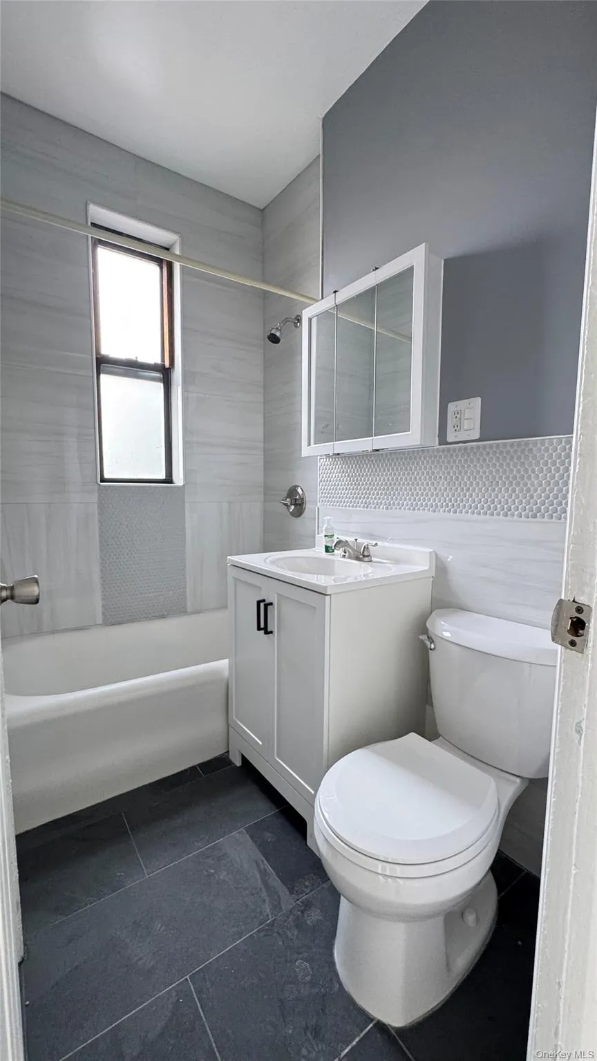 Bathroom with vanity, shower / bath combination, wainscoting, and tile walls Bathroom with vanity, shower / bath combination, wainscoting, and tile walls