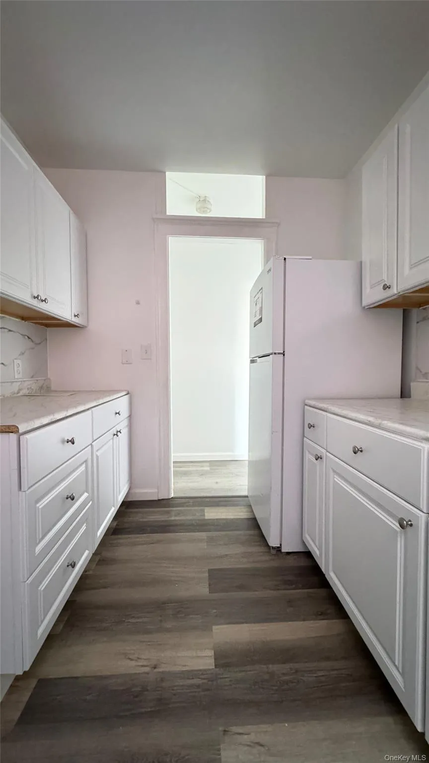 Kitchen featuring white cabinetry, light countertops, freestanding refrigerator, and dark wood-type flooring Kitchen featuring white cabinetry, light countertops, freestanding refrigerator, and dark wood-type flooring