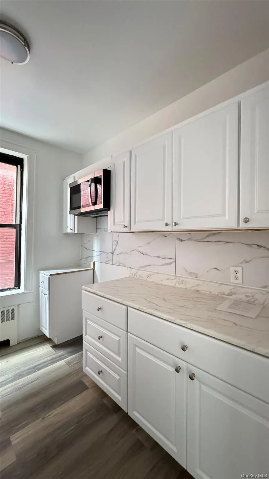 Kitchen with tasteful backsplash, light countertops, white cabinetry, and dark wood-style floors Kitchen with tasteful backsplash, light countertops, white cabinetry, and dark wood-style floors
