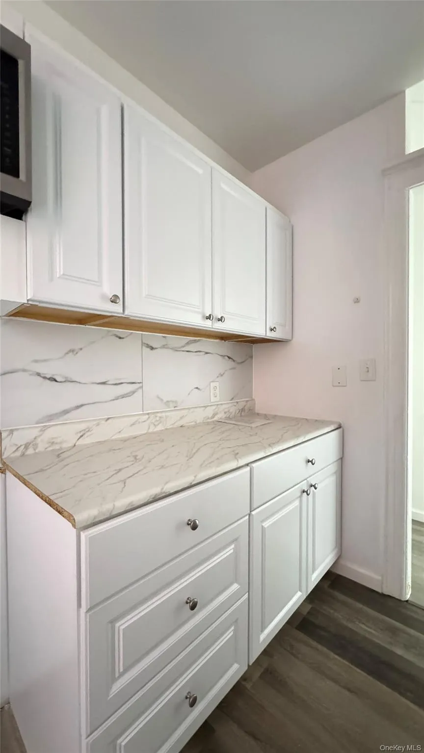 Kitchen featuring white cabinetry, dark wood-style flooring, backsplash, and stainless steel microwave Kitchen featuring white cabinetry, dark wood-style flooring, backsplash, and stainless steel microwave