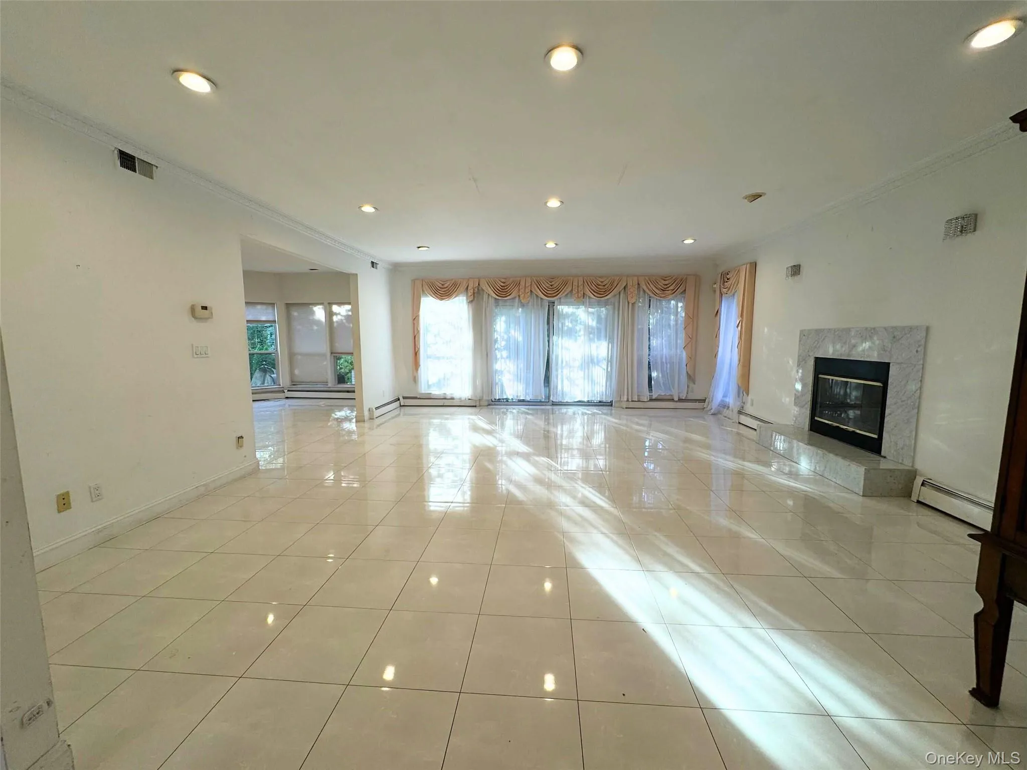 Unfurnished living room featuring crown molding, a premium fireplace, recessed lighting, light tile patterned floors, and baseboard heating Unfurnished living room featuring crown molding, a premium fireplace, recessed lighting, light tile patterned floors, and baseboard heating