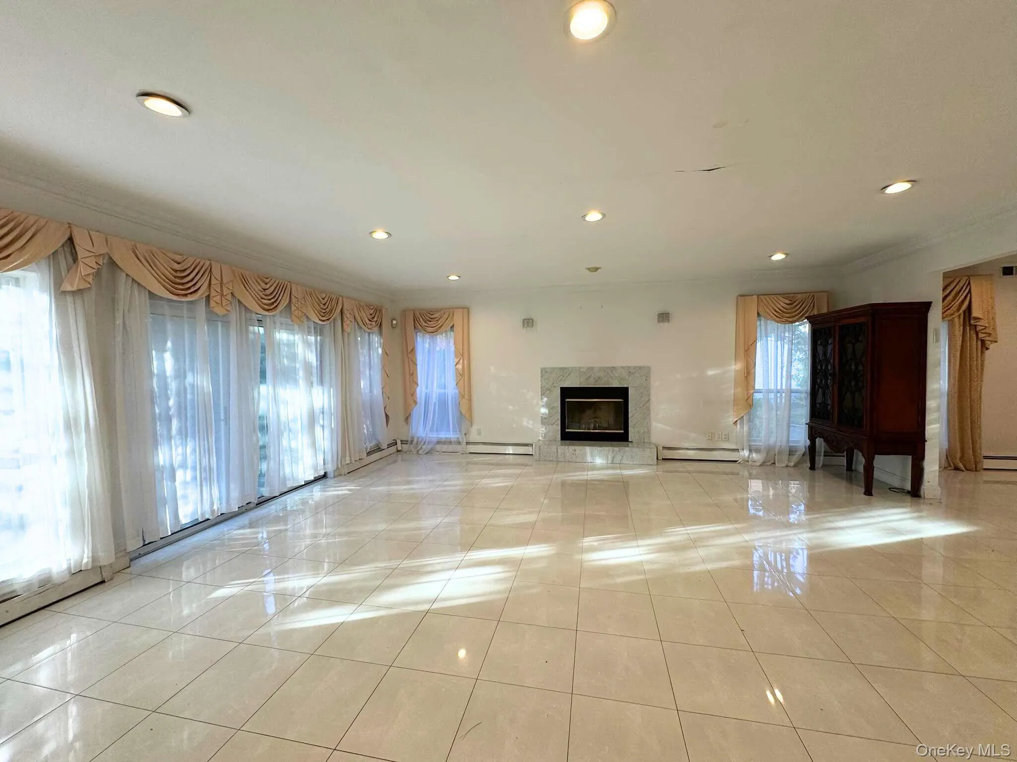 Unfurnished living room with a high end fireplace, recessed lighting, light tile patterned floors, ornamental molding, and a baseboard heating unit Unfurnished living room with a high end fireplace, recessed lighting, light tile patterned floors, ornamental molding, and a baseboard heating unit