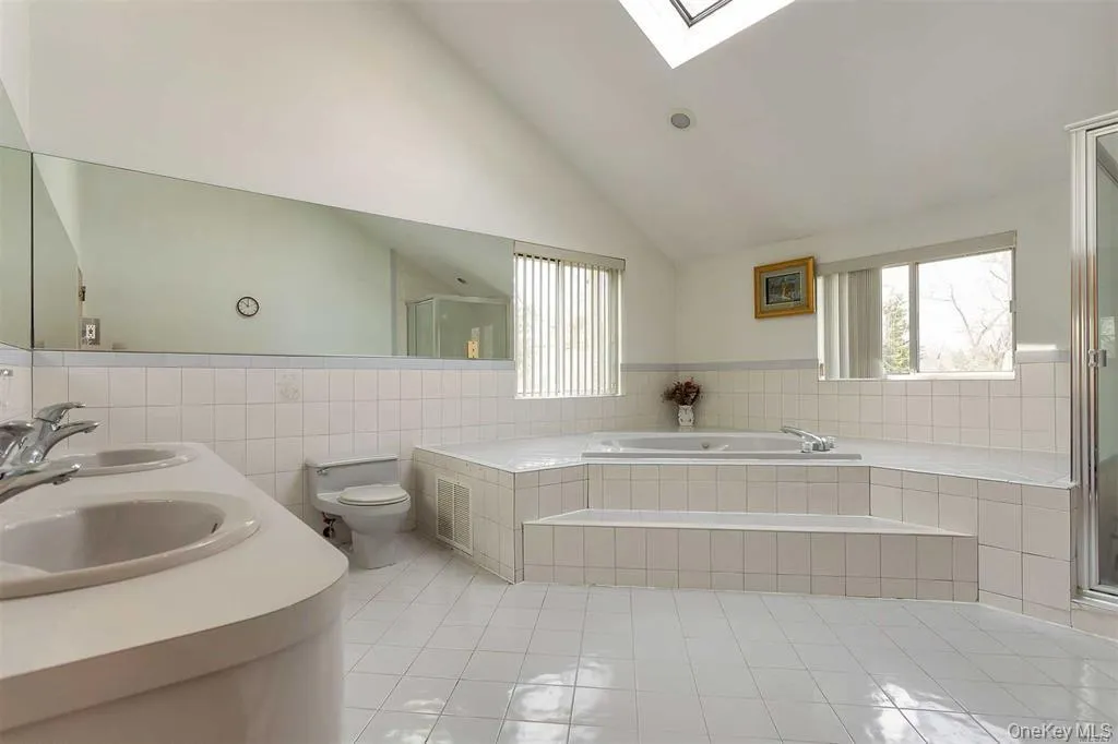 Full bathroom featuring light tile patterned flooring, a skylight, a bath, tile walls, and double vanity Full bathroom featuring light tile patterned flooring, a skylight, a bath, tile walls, and double vanity