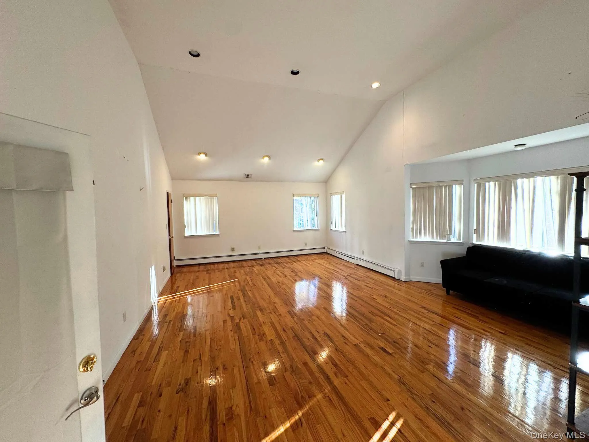 Unfurnished living room with wood-type flooring, high vaulted ceiling, baseboard heating, and recessed lighting Unfurnished living room with wood-type flooring, high vaulted ceiling, baseboard heating, and recessed lighting