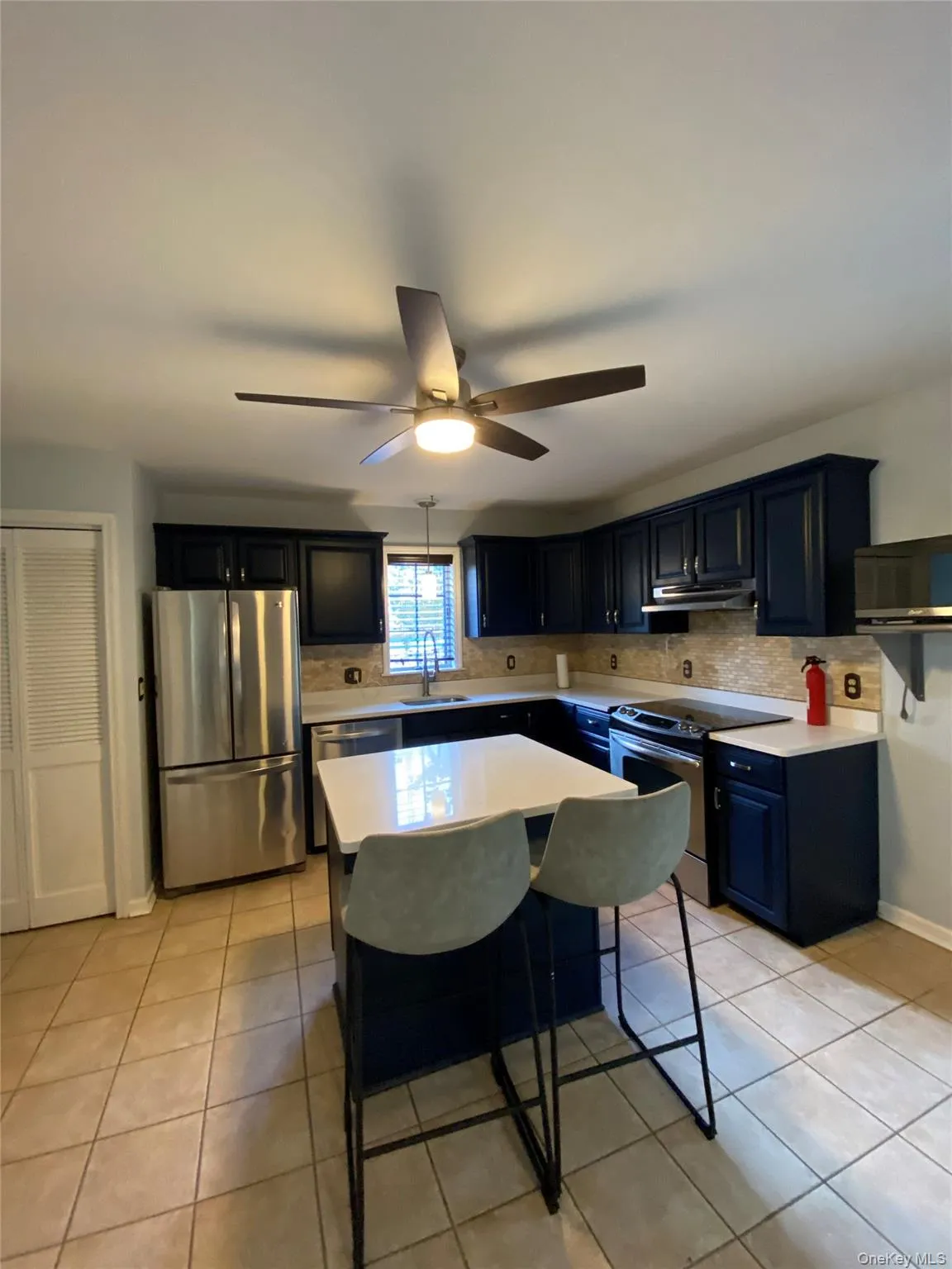 Kitchen featuring appliances with stainless steel finishes, light countertops, backsplash, and light tile patterned flooring Kitchen featuring appliances with stainless steel finishes, light countertops, backsplash, and light tile patterned flooring