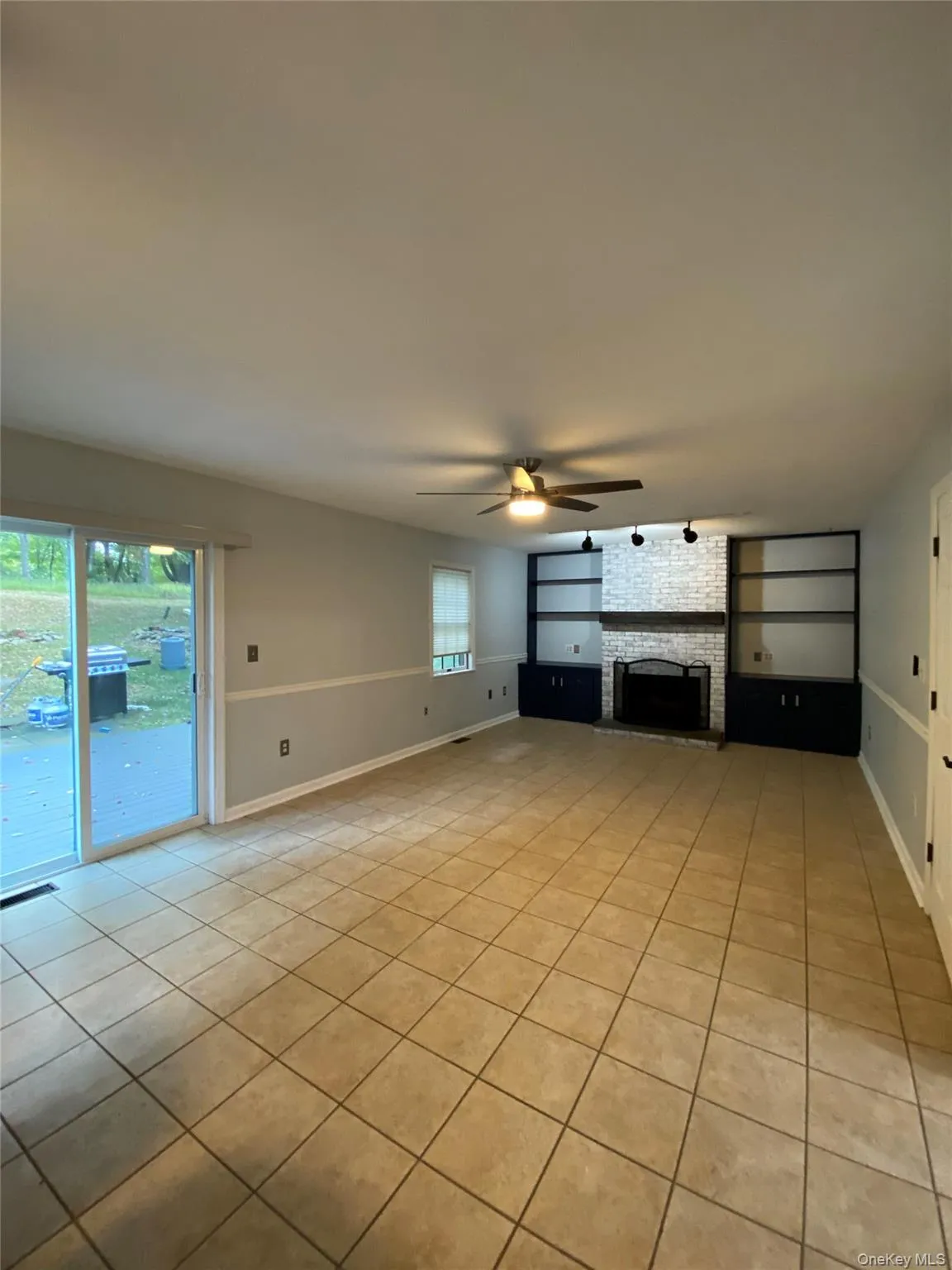 Unfurnished living room featuring light tile patterned floors, a brick fireplace, and a ceiling fan Unfurnished living room featuring light tile patterned floors, a brick fireplace, and a ceiling fan