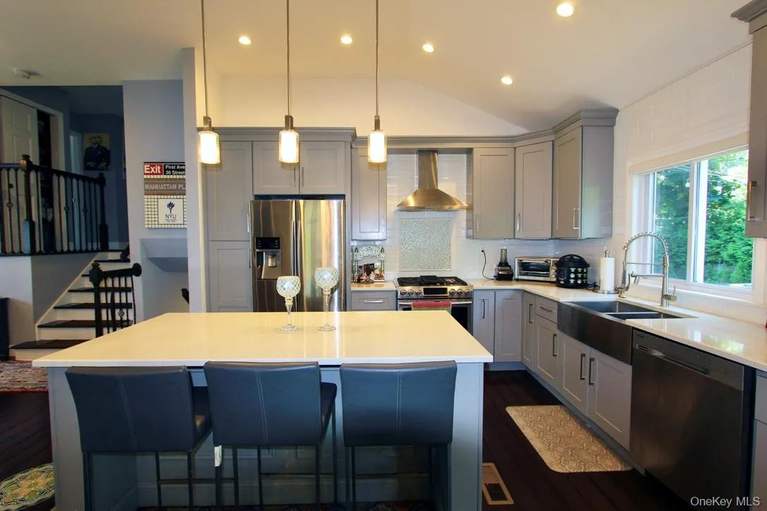 Kitchen with gray cabinetry, a kitchen breakfast bar, stainless steel appliances, decorative backsplash, and ventilation hood Kitchen with gray cabinetry, a kitchen breakfast bar, stainless steel appliances, decorative backsplash, and ventilation hood