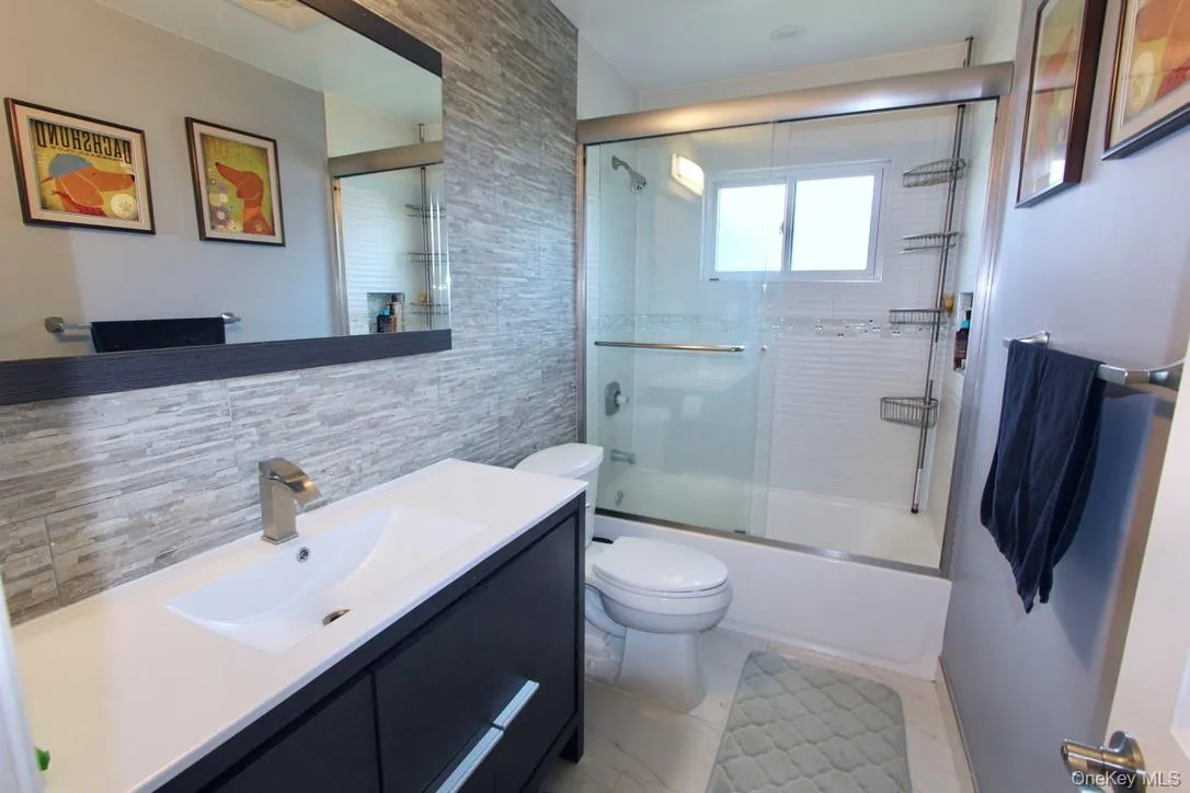 Full bath featuring vanity, shower / bath combination with glass door, tile walls, and decorative backsplash Full bath featuring vanity, shower / bath combination with glass door, tile walls, and decorative backsplash