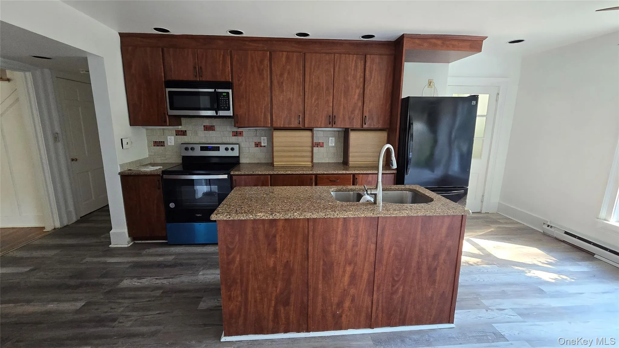 Kitchen featuring appliances with stainless steel finishes, decorative backsplash, dark wood finished floors, and light stone countertops Kitchen featuring appliances with stainless steel finishes, decorative backsplash, dark wood finished floors, and light stone countertops