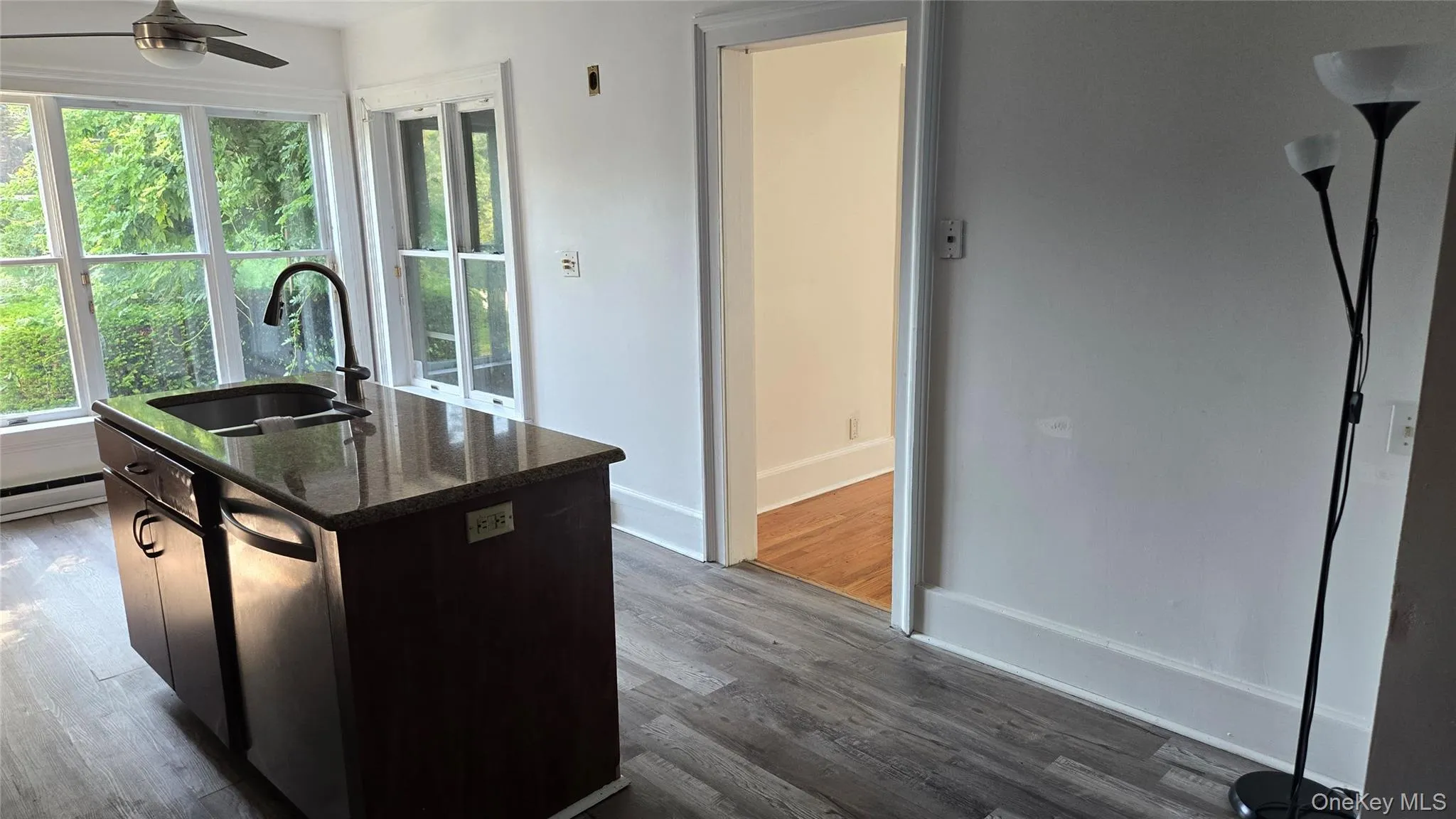 Kitchen featuring dark stone counters, dark wood-style flooring, a center island with sink, stainless steel dishwasher, and dark brown cabinetry Kitchen featuring dark stone counters, dark wood-style flooring, a center island with sink, stainless steel dishwasher, and dark brown cabinetry