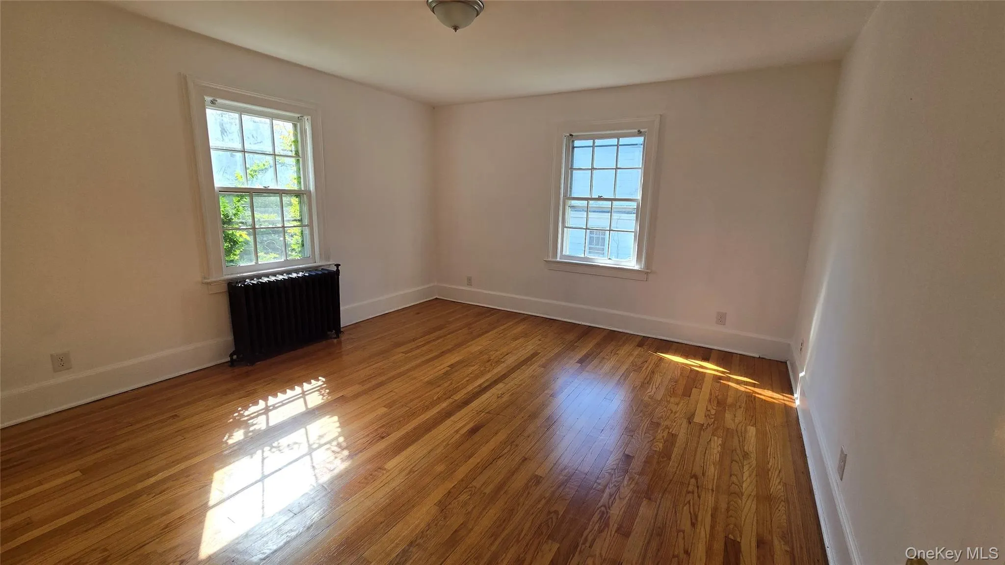 Empty room featuring radiator and hardwood / wood-style floors Empty room featuring radiator and hardwood / wood-style floors