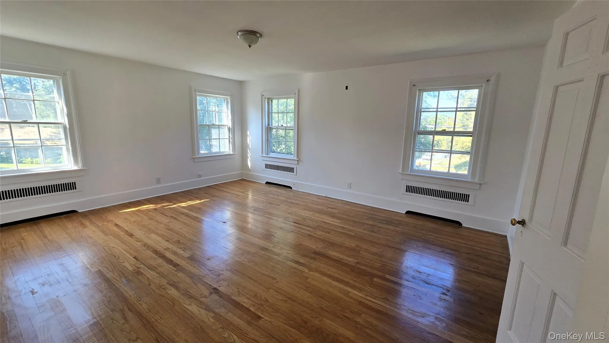 Spare room with plenty of natural light, wood finished floors, and radiator Spare room with plenty of natural light, wood finished floors, and radiator