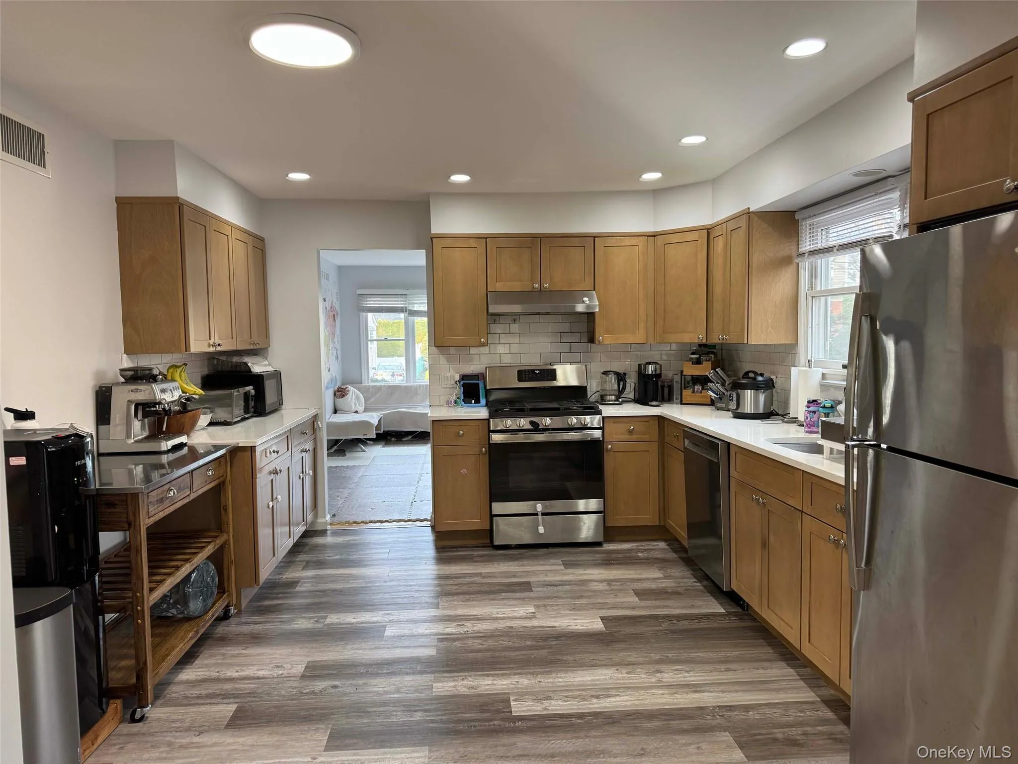 Kitchen featuring appliances with stainless steel finishes, tasteful backsplash, brown cabinets, dark wood-type flooring, and recessed lighting Kitchen featuring appliances with stainless steel finishes, tasteful backsplash, brown cabinets, dark wood-type flooring, and recessed lighting