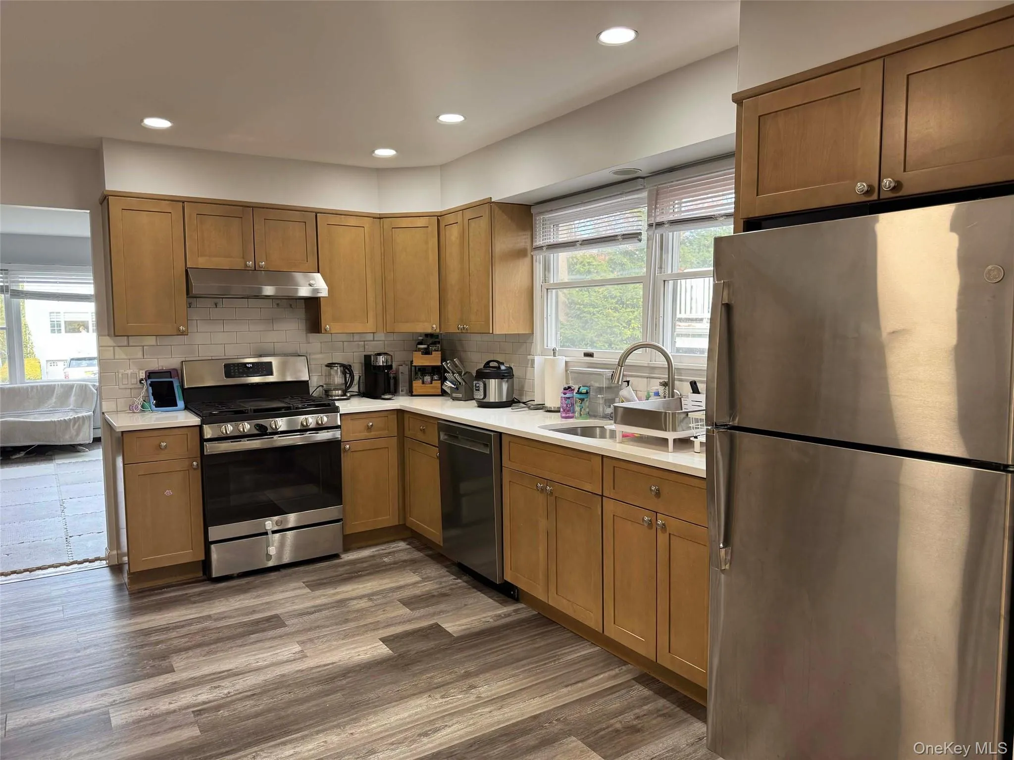 Kitchen with appliances with stainless steel finishes, brown cabinets, tasteful backsplash, recessed lighting, and dark wood-type flooring Kitchen with appliances with stainless steel finishes, brown cabinets, tasteful backsplash, recessed lighting, and dark wood-type flooring
