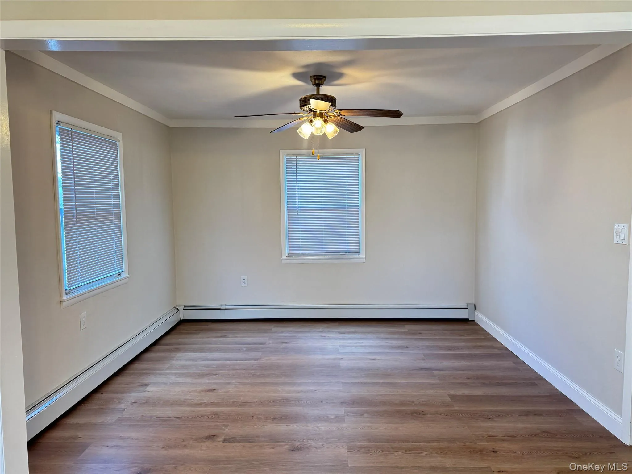 Spare room featuring a baseboard heating unit, light wood-style floors, ornamental molding, and a ceiling fan Spare room featuring a baseboard heating unit, light wood-style floors, ornamental molding, and a ceiling fan