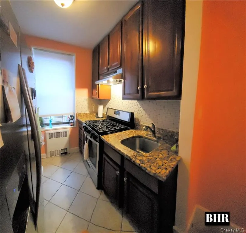 Kitchen with stainless steel appliances, light stone countertops, light tile patterned floors, under cabinet range hood, and tasteful backsplash Kitchen with stainless steel appliances, light stone countertops, light tile patterned floors, under cabinet range hood, and tasteful backsplash