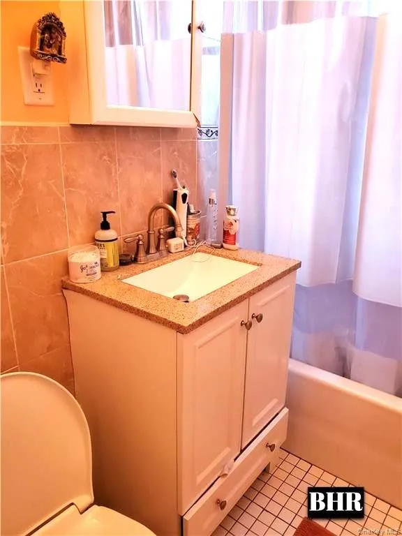 Full bath with vanity, shower / tub combo with curtain, tile walls, tasteful backsplash, and light tile patterned floors Full bath with vanity, shower / tub combo with curtain, tile walls, tasteful backsplash, and light tile patterned floors