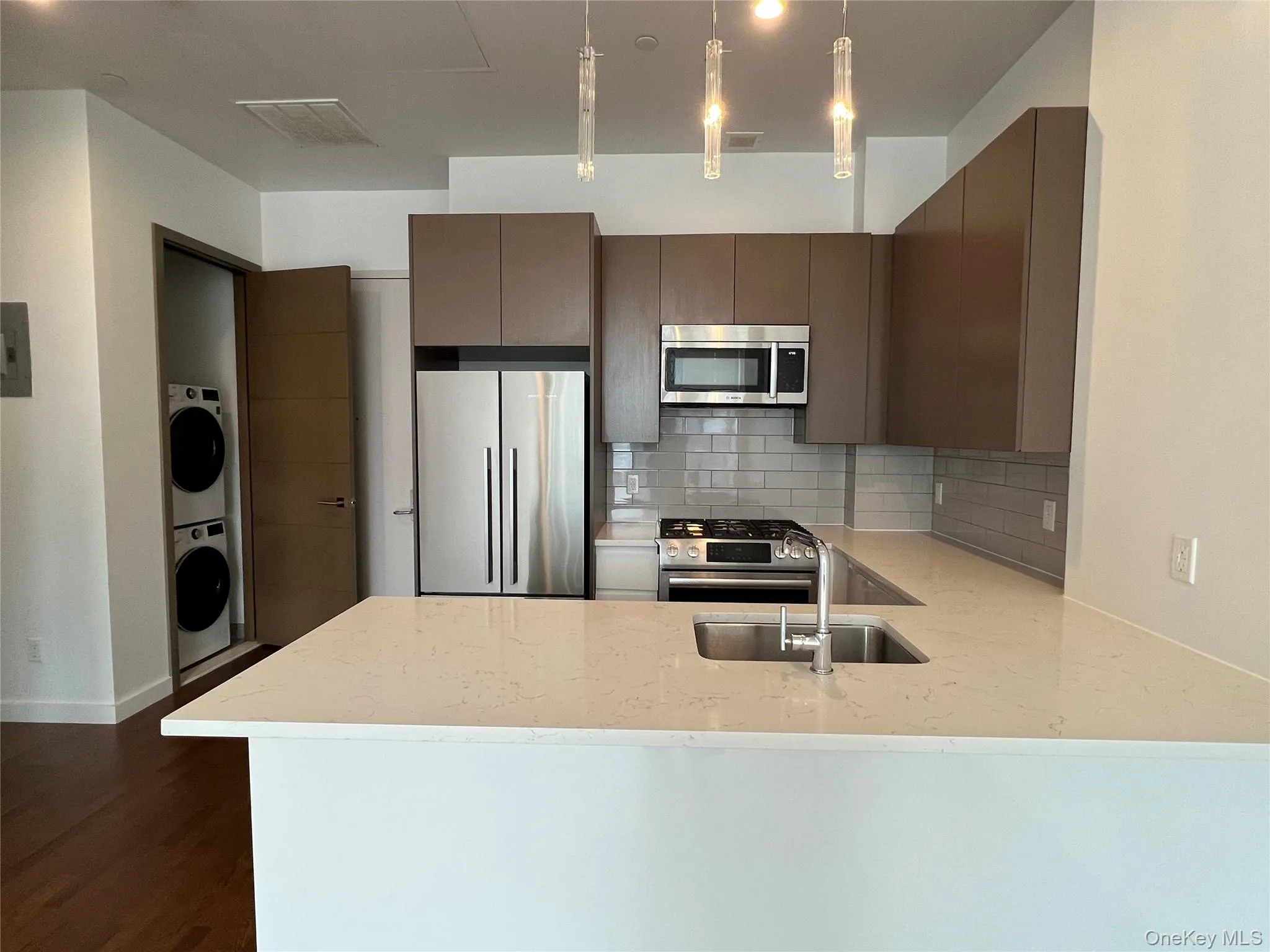 Kitchen featuring stainless steel appliances, pendant lighting, decorative backsplash, light stone counters, and a peninsula Kitchen featuring stainless steel appliances, pendant lighting, decorative backsplash, light stone counters, and a peninsula