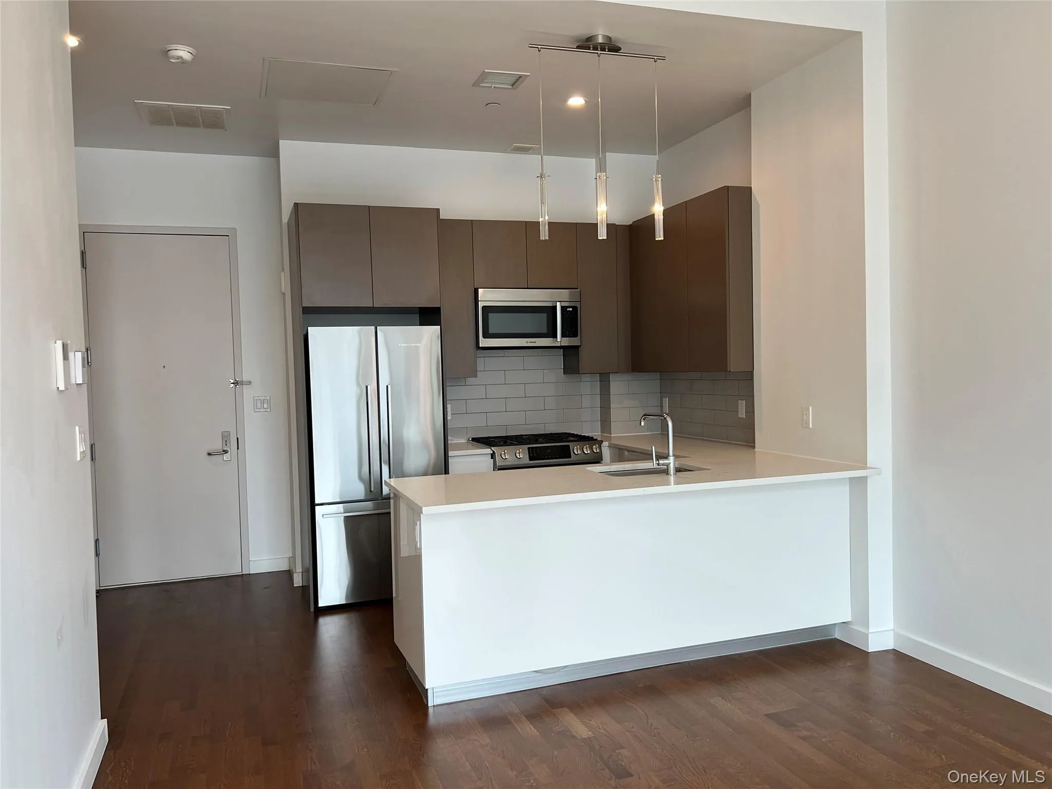 Kitchen with stainless steel appliances, backsplash, hanging light fixtures, a peninsula, and dark wood-style flooring Kitchen with stainless steel appliances, backsplash, hanging light fixtures, a peninsula, and dark wood-style flooring