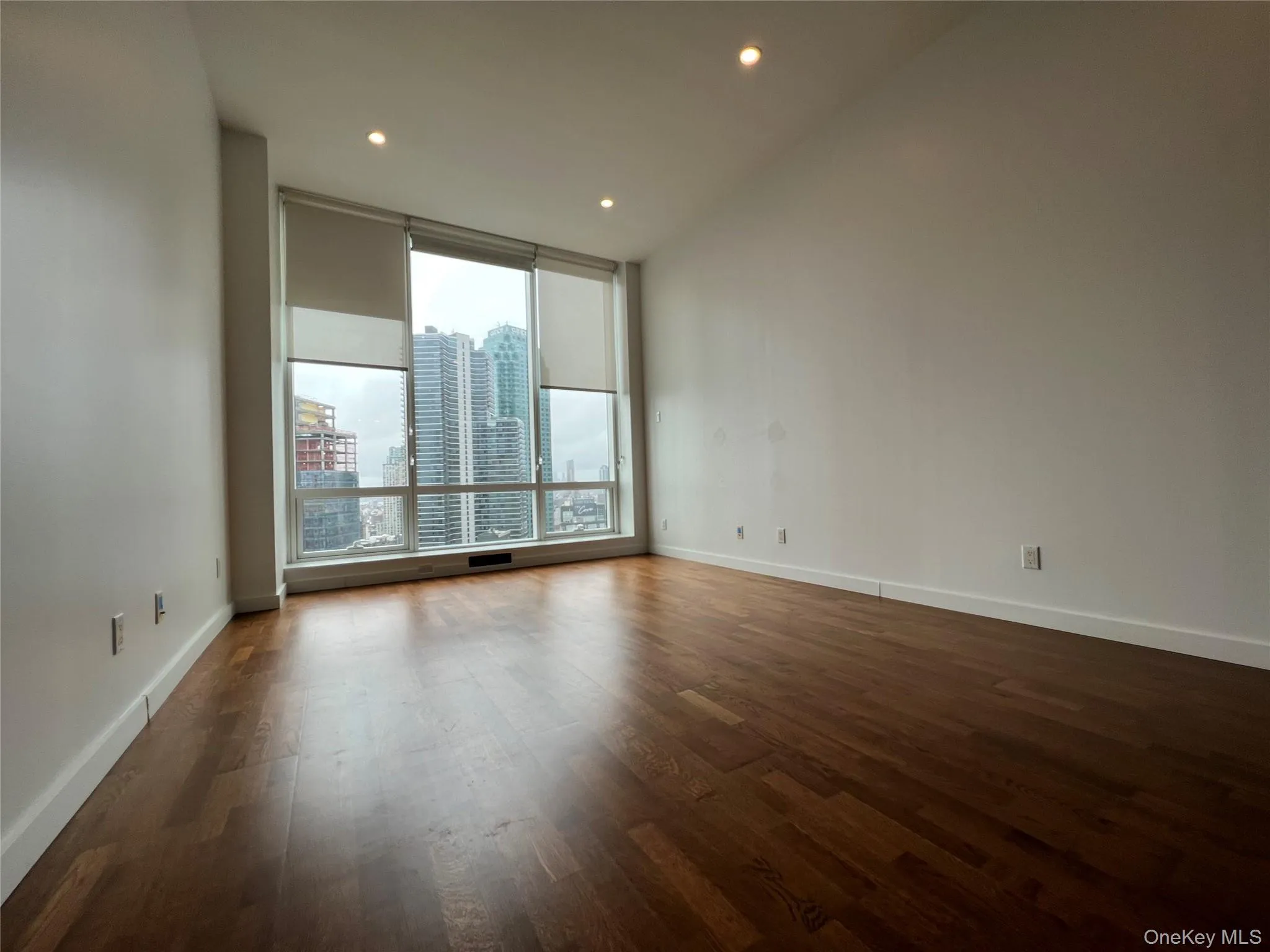 Spare room with a view of city, dark wood finished floors, recessed lighting, and floor to ceiling windows Spare room with a view of city, dark wood finished floors, recessed lighting, and floor to ceiling windows