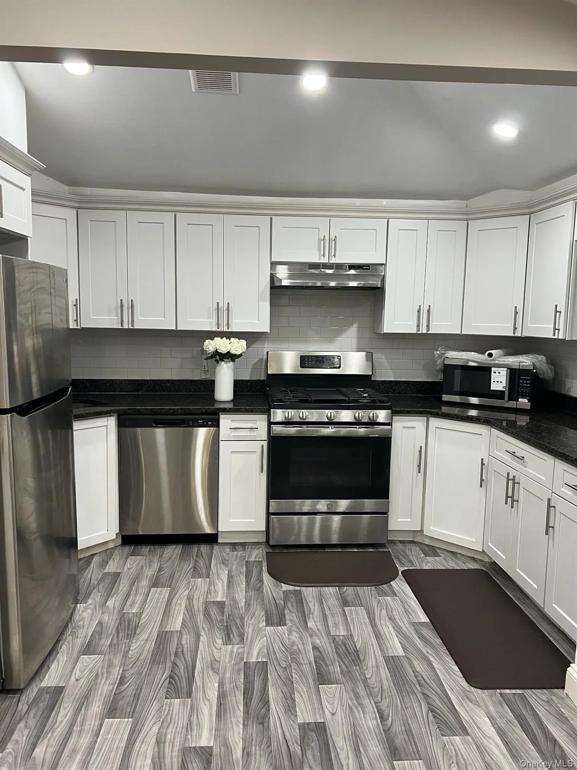 Kitchen with appliances with stainless steel finishes, backsplash, recessed lighting, white cabinets, and light wood-style flooring Kitchen with appliances with stainless steel finishes, backsplash, recessed lighting, white cabinets, and light wood-style flooring