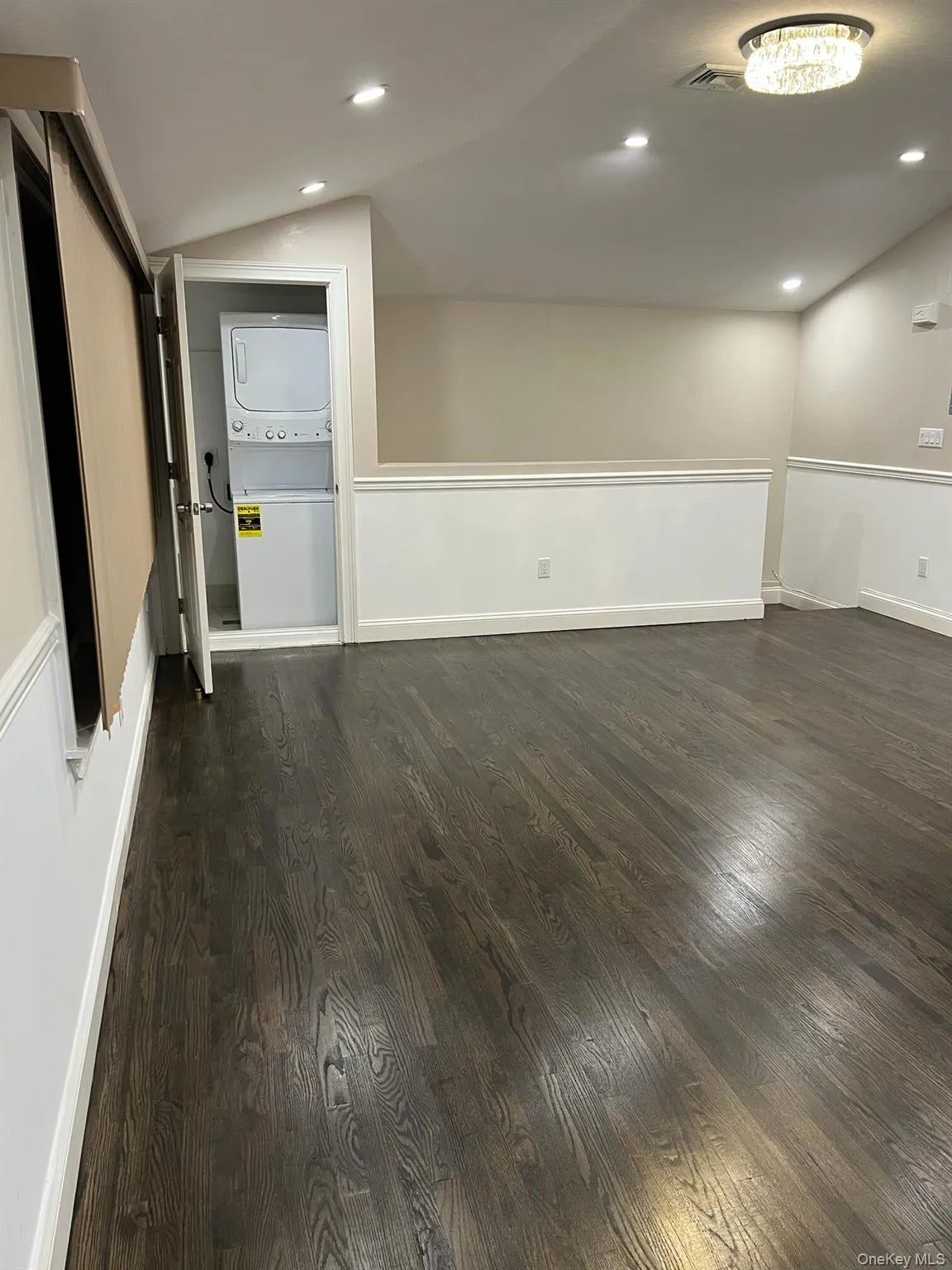 Empty room with recessed lighting, dark wood finished floors, stacked washing machine and dryer, and lofted ceiling Empty room with recessed lighting, dark wood finished floors, stacked washing machine and dryer, and lofted ceiling