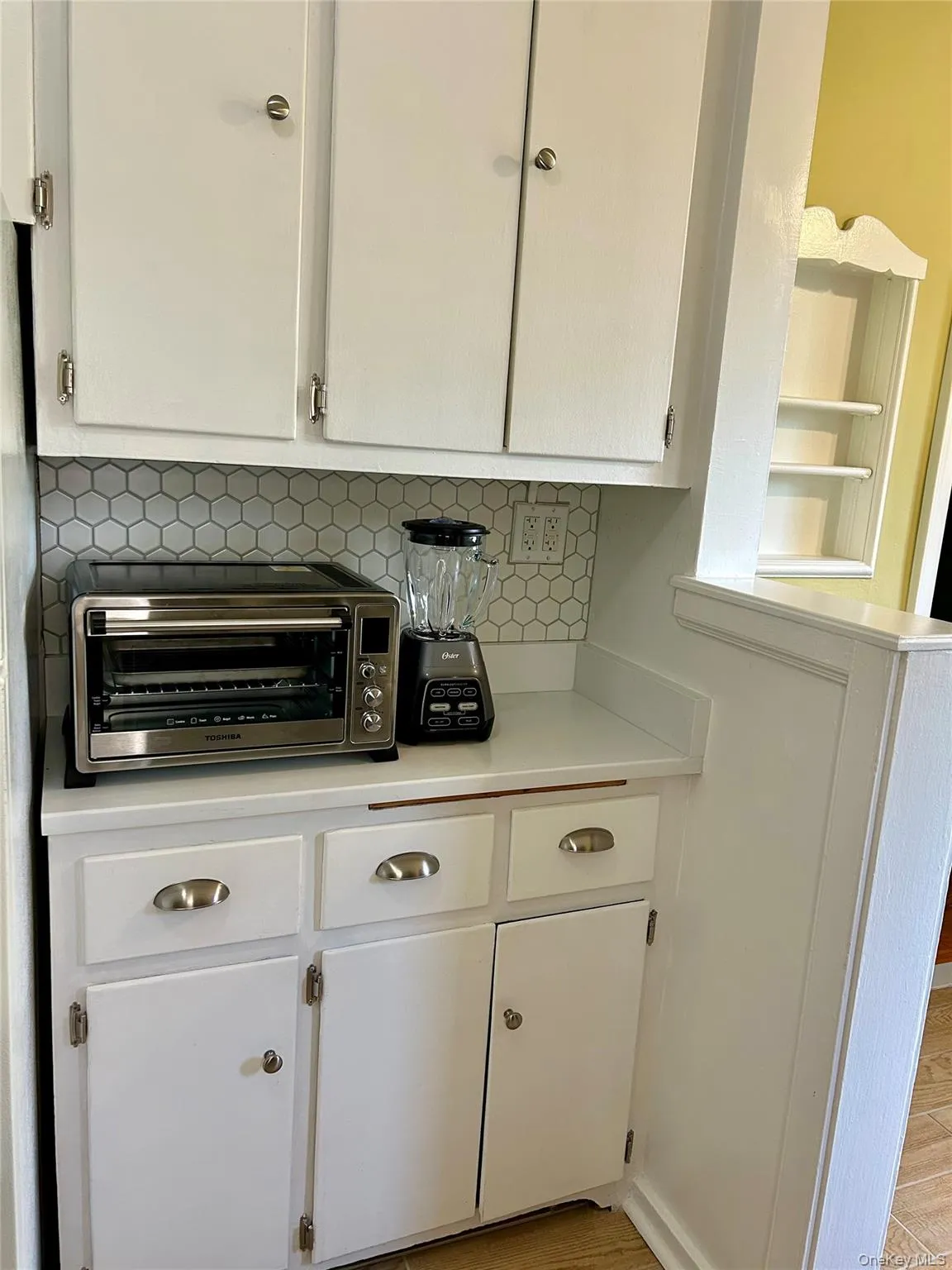 Kitchen view of white cabinets, light countertops, decorative backsplash, light appliances, and open shelves Kitchen view of white cabinets, light countertops, decorative backsplash, light appliances, and open shelves
