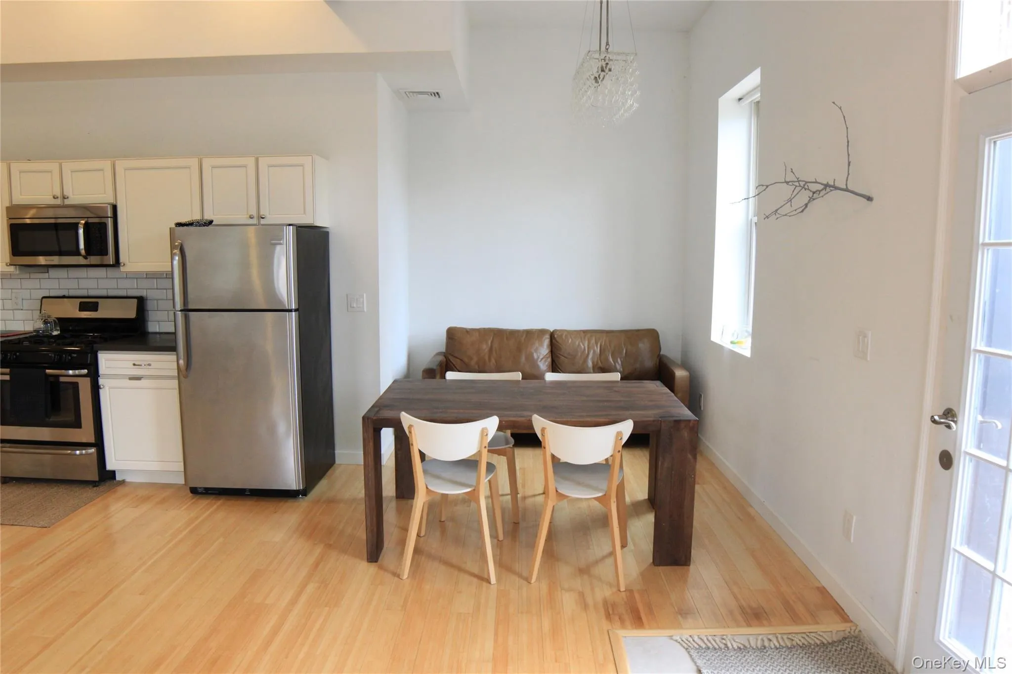 Kitchen with stainless steel appliances, tasteful backsplash, white cabinetry, light wood-style floors, and decorative light fixtures Kitchen with stainless steel appliances, tasteful backsplash, white cabinetry, light wood-style floors, and decorative light fixtures