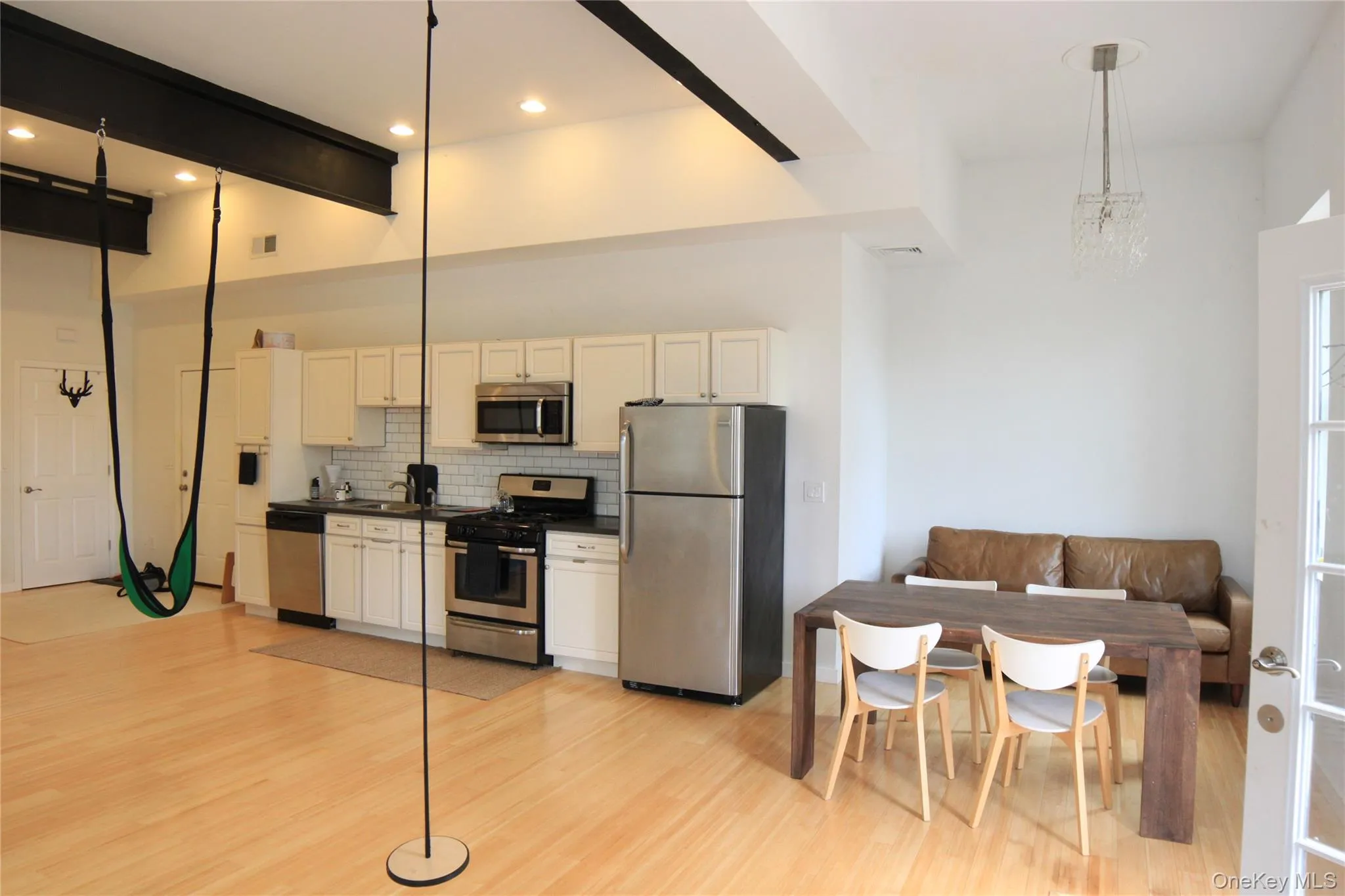 Kitchen featuring appliances with stainless steel finishes, tasteful backsplash, light wood-style flooring, white cabinetry, and dark countertops Kitchen featuring appliances with stainless steel finishes, tasteful backsplash, light wood-style flooring, white cabinetry, and dark countertops