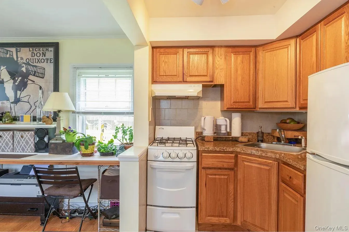 Kitchen featuring white appliances, brown cabinets, decorative backsplash, under cabinet range hood, and ornamental molding Kitchen featuring white appliances, brown cabinets, decorative backsplash, under cabinet range hood, and ornamental molding