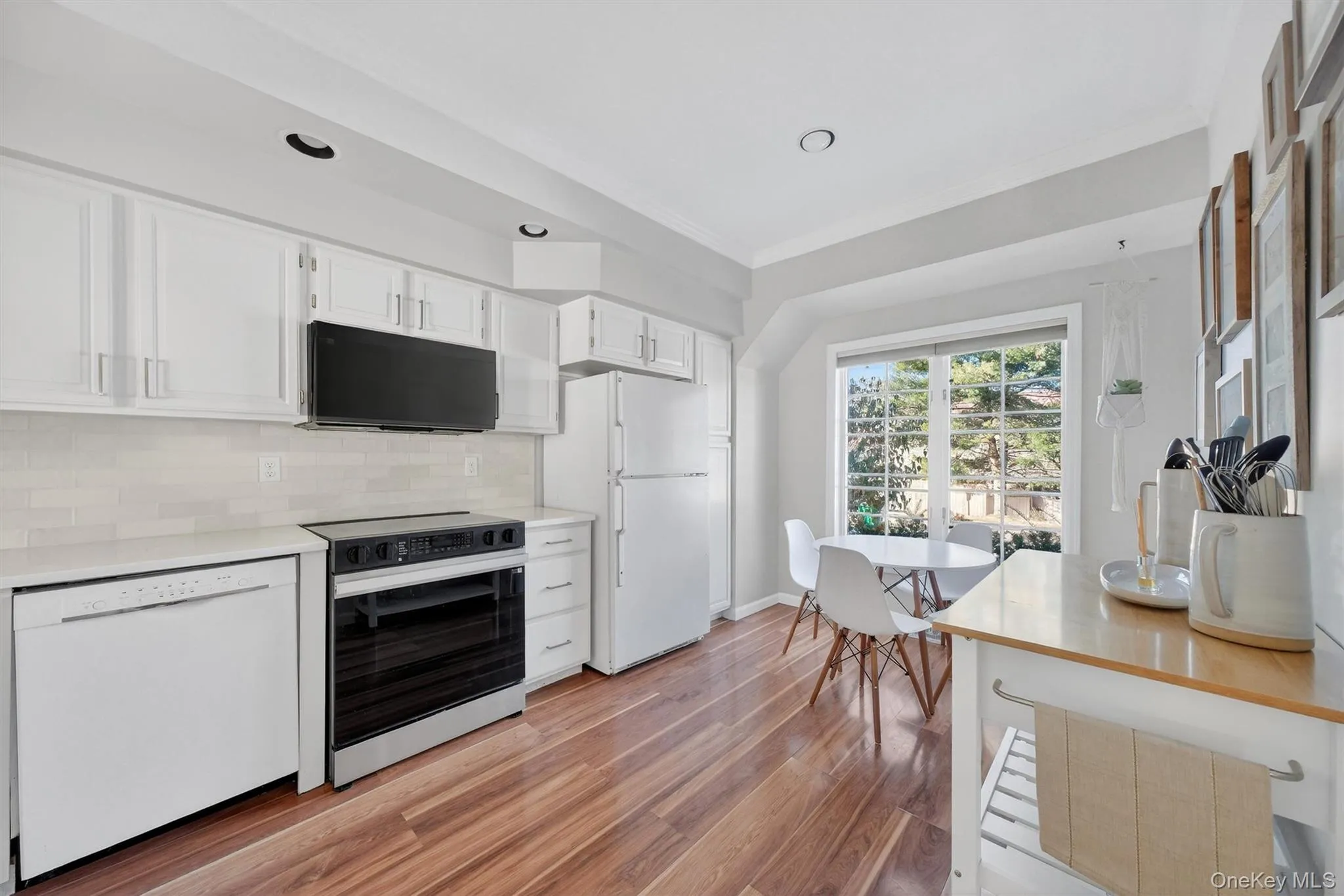 Kitchen with white cabinetry, black appliances, decorative backsplash, crown molding, and light wood-type flooring Kitchen with white cabinetry, black appliances, decorative backsplash, crown molding, and light wood-type flooring